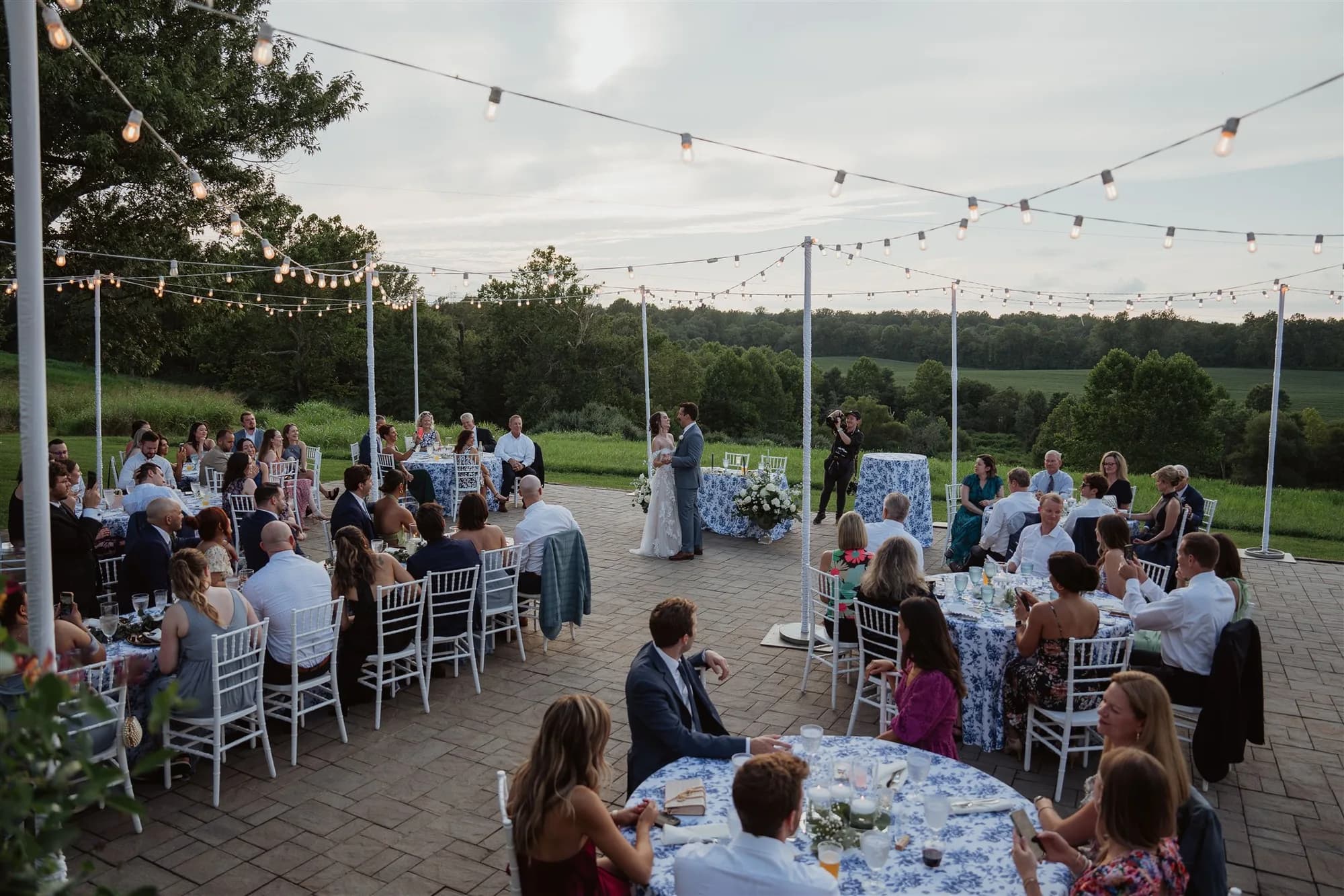 Outdoor reception on Rixey Manor terrace with string lights, blue floral linens, and rolling Virginia countryside at dusk