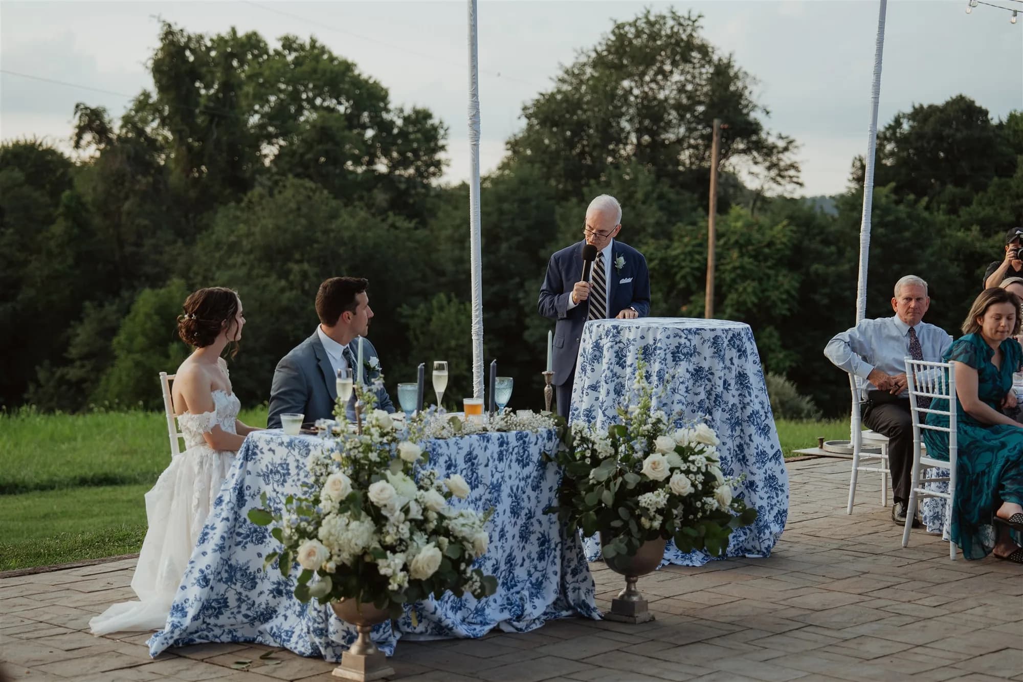 Toast speech at sweetheart table on Rixey Manor terrace at dusk with blue floral linens and white garden florals