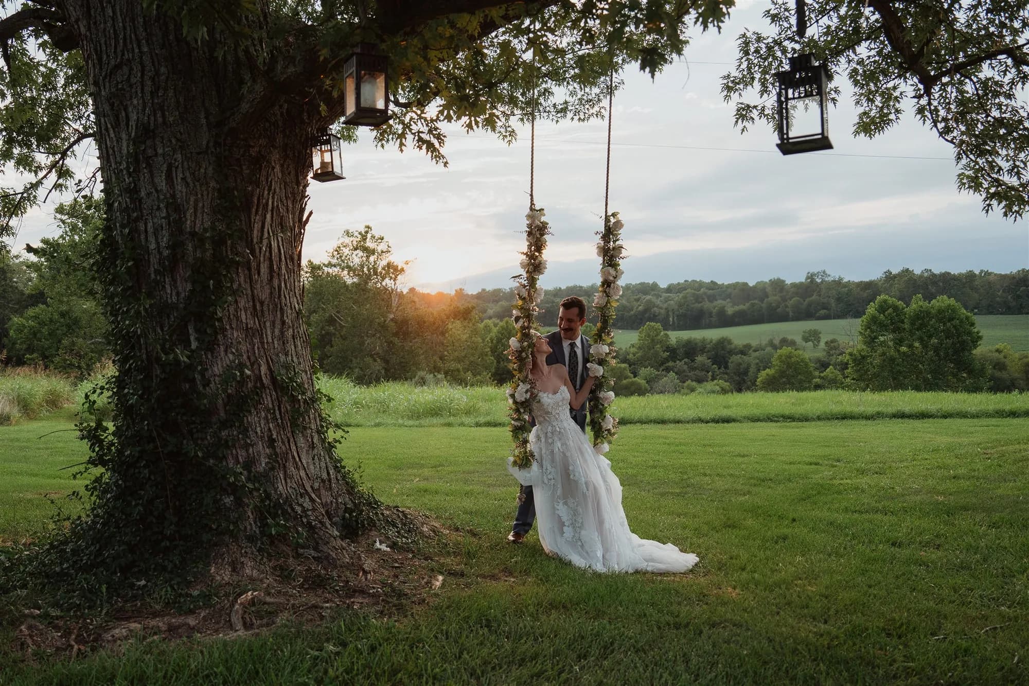 Bride and groom share a tender moment on a floral swing beneath a grand oak tree at golden hour at Rixey Manor