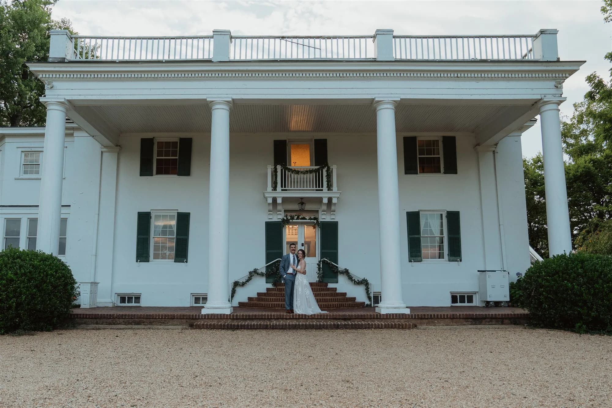 Bride and groom pose on the grand front steps of Rixey Manor's white columned historic estate at dusk