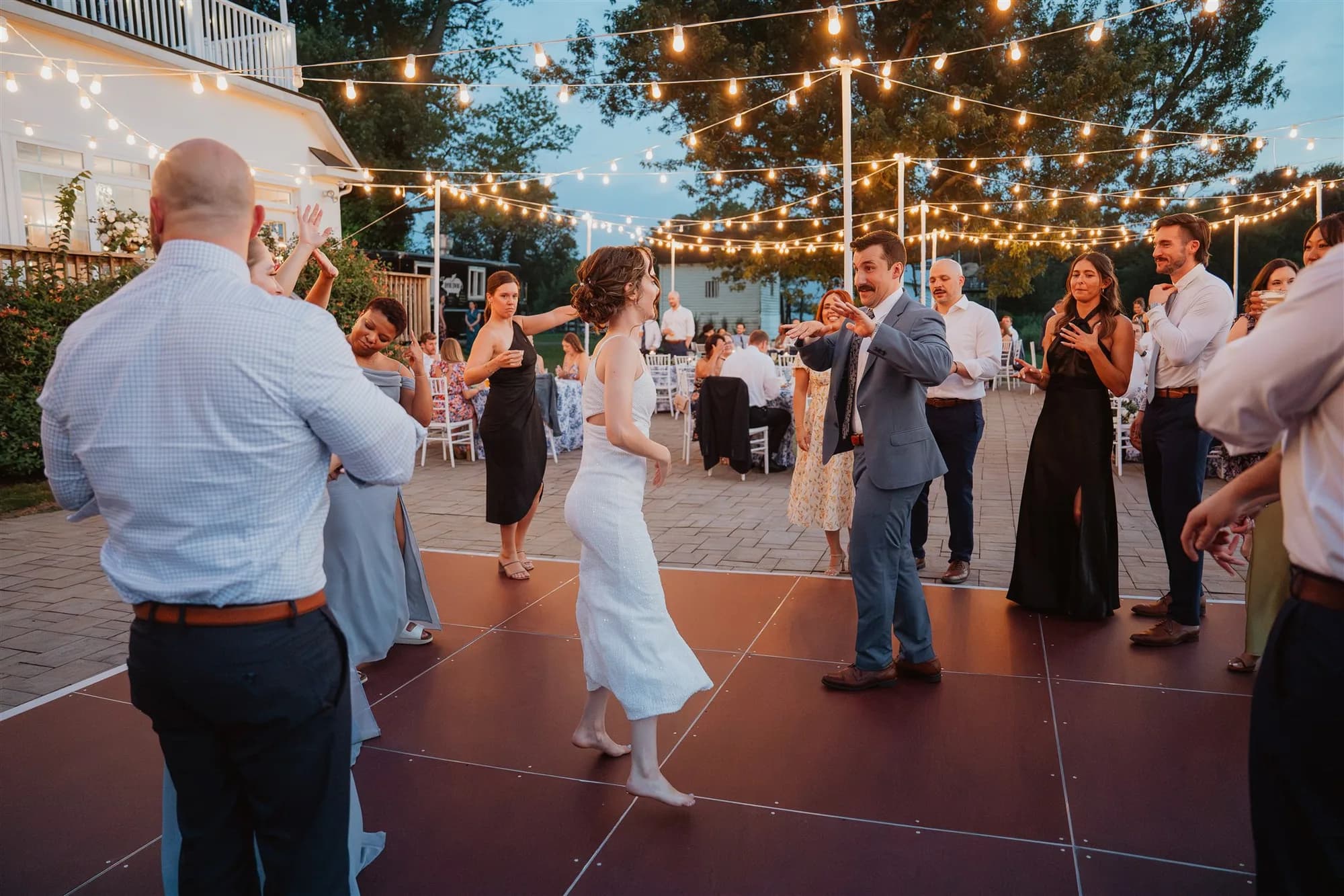 Bride and groom dance under string lights on outdoor patio at Rixey Manor reception as guests cheer