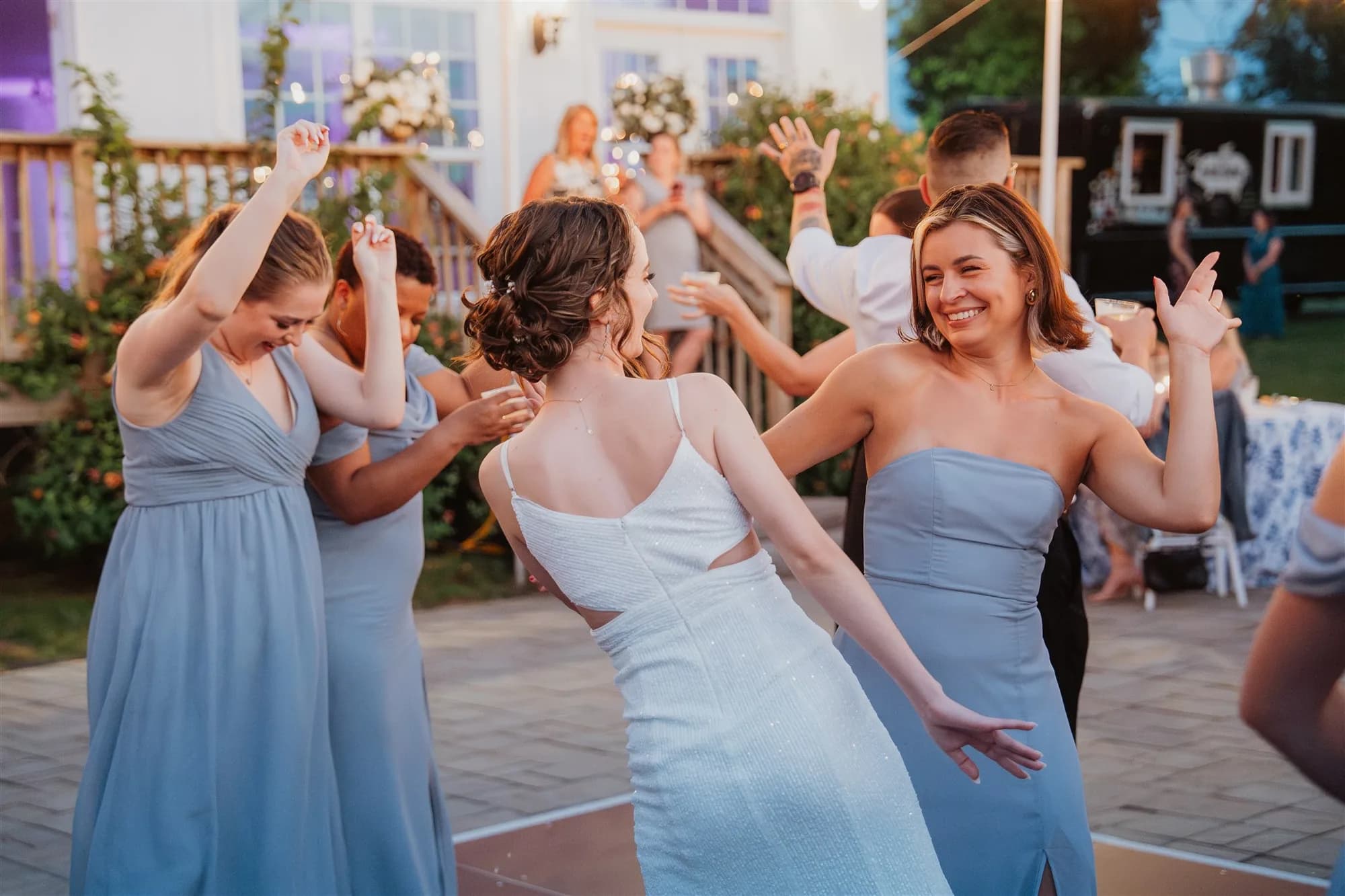 Bride dancing joyfully with bridesmaids in blue gowns at outdoor wedding reception