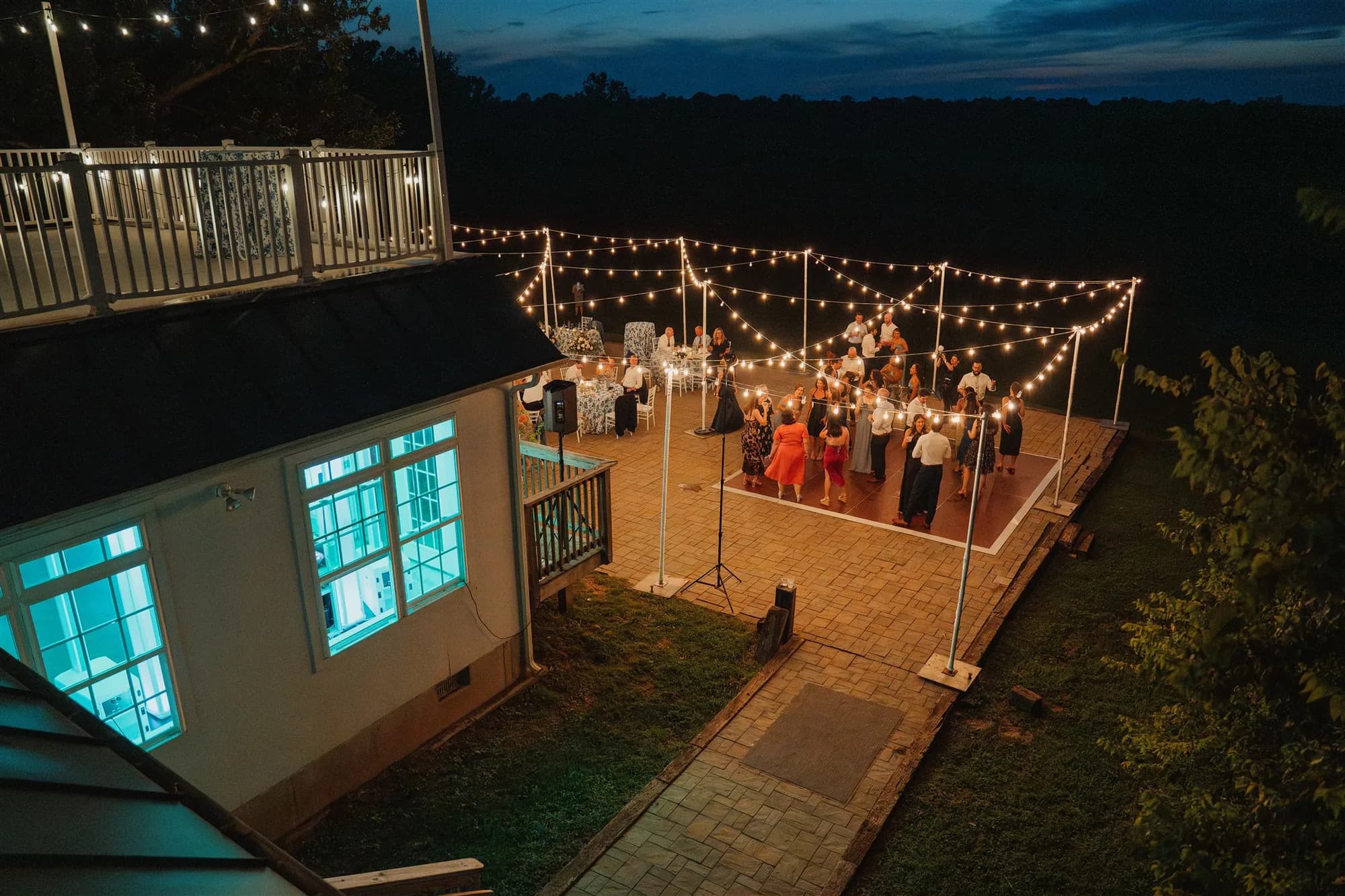 Guests dancing under string lights on outdoor patio at Rixey Manor at dusk, venue and grounds visible
