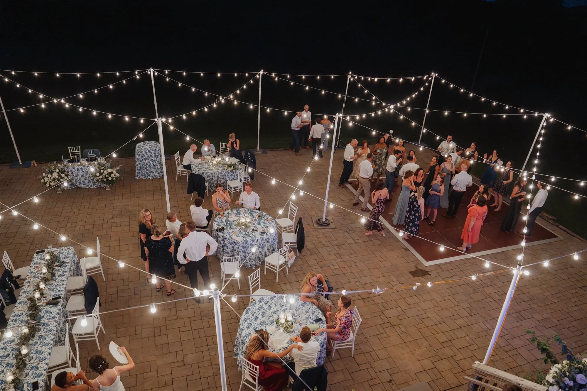Aerial night view of outdoor wedding reception at Rixey Manor with string lights over brick patio and dancing guests