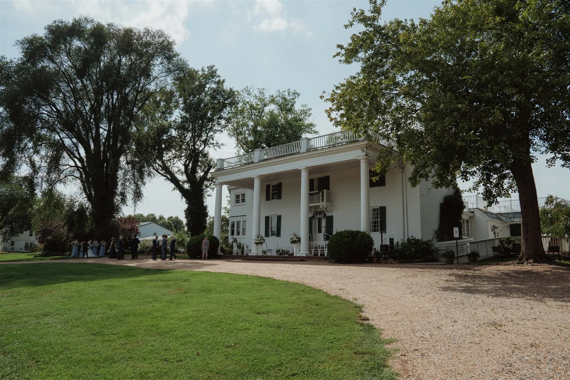 Wide view of Rixey Manor's white columned estate with guests gathering on the lawn during a summer wedding