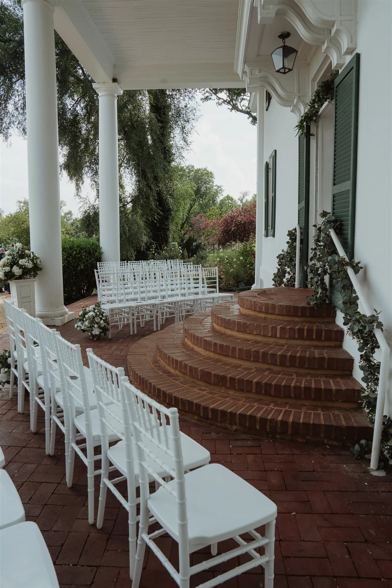 White chiavari chairs arranged for a ceremony on the brick portico of a historic white-columned Virginia manor
