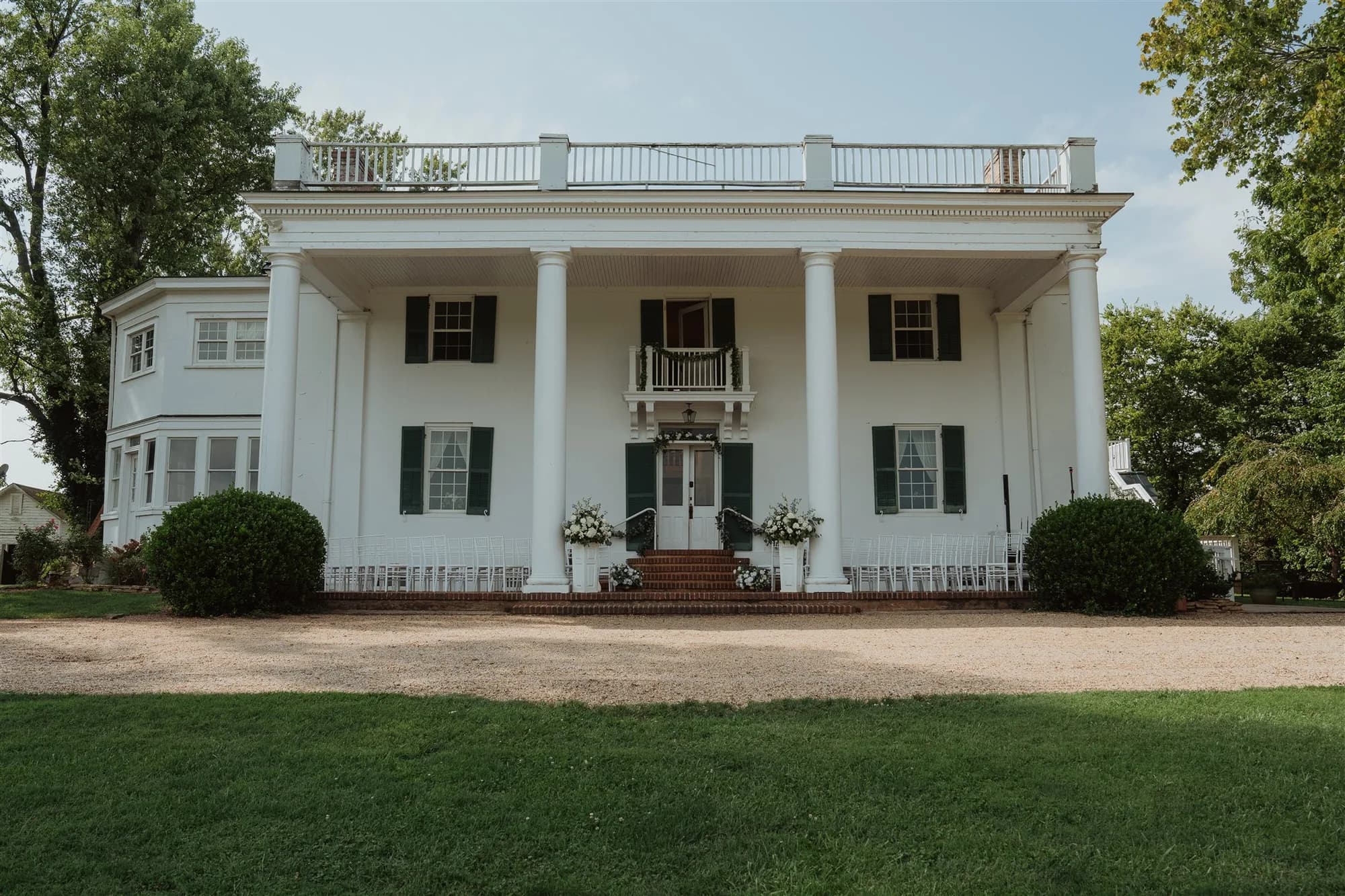 Front facade of Rixey Manor estate showing white columned portico, green shutters, and floral-lined entrance steps