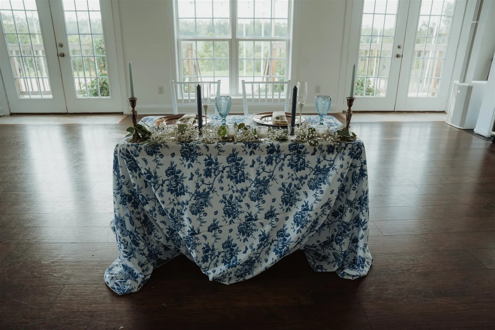 Blue floral tablecloth draped over sweetheart table with taper candles near French doors at Rixey Manor
