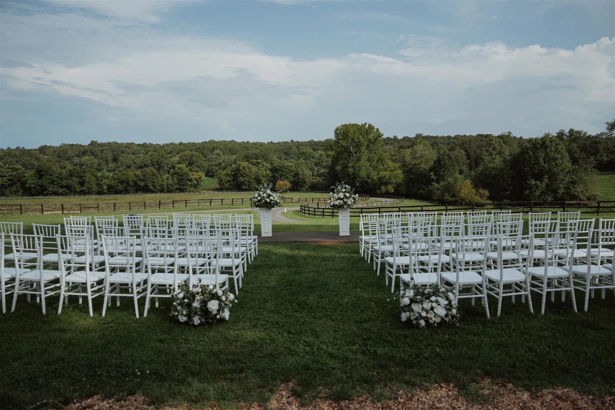 Outdoor ceremony setup with white Chiavari chairs and floral arrangements on Rixey Manor's green lawn