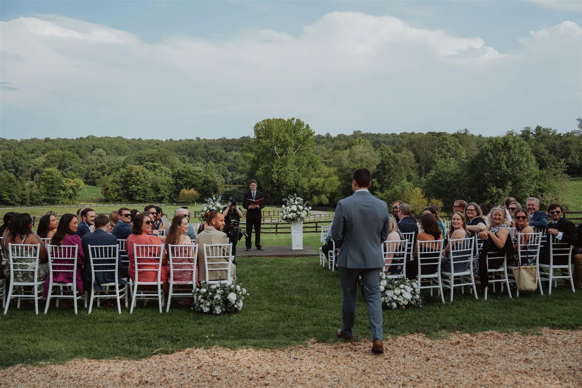 Groom walks down the aisle at an outdoor ceremony on Rixey Manor's sunlit grounds with wooded backdrop