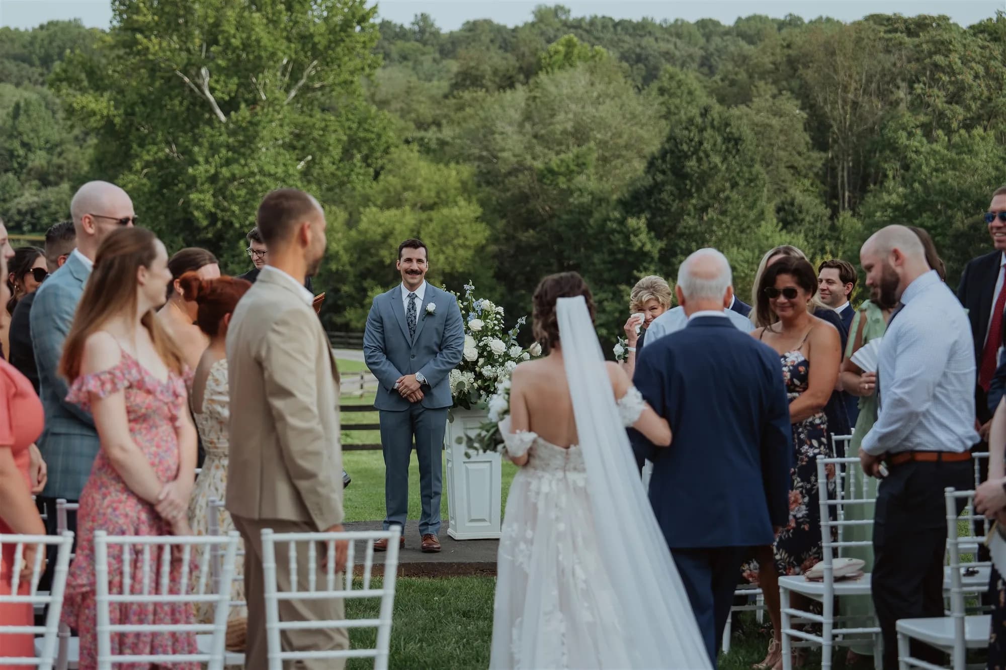 Groom watches bride walk down outdoor aisle at Rixey Manor ceremony amid lush Virginia greenery