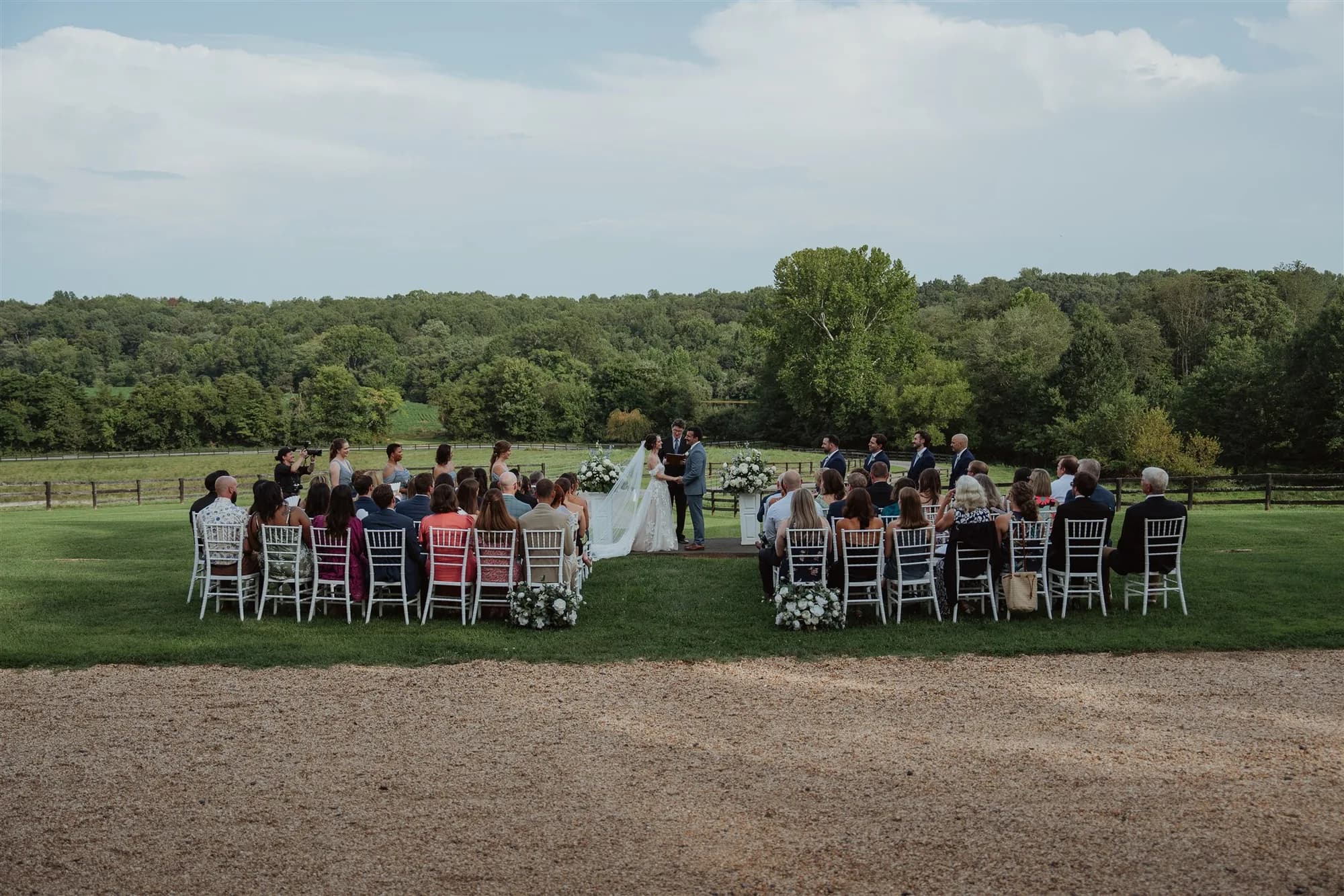 Outdoor wedding ceremony on lush green lawn at Rixey Manor, guests seated in white chairs amid rolling Virginia countryside