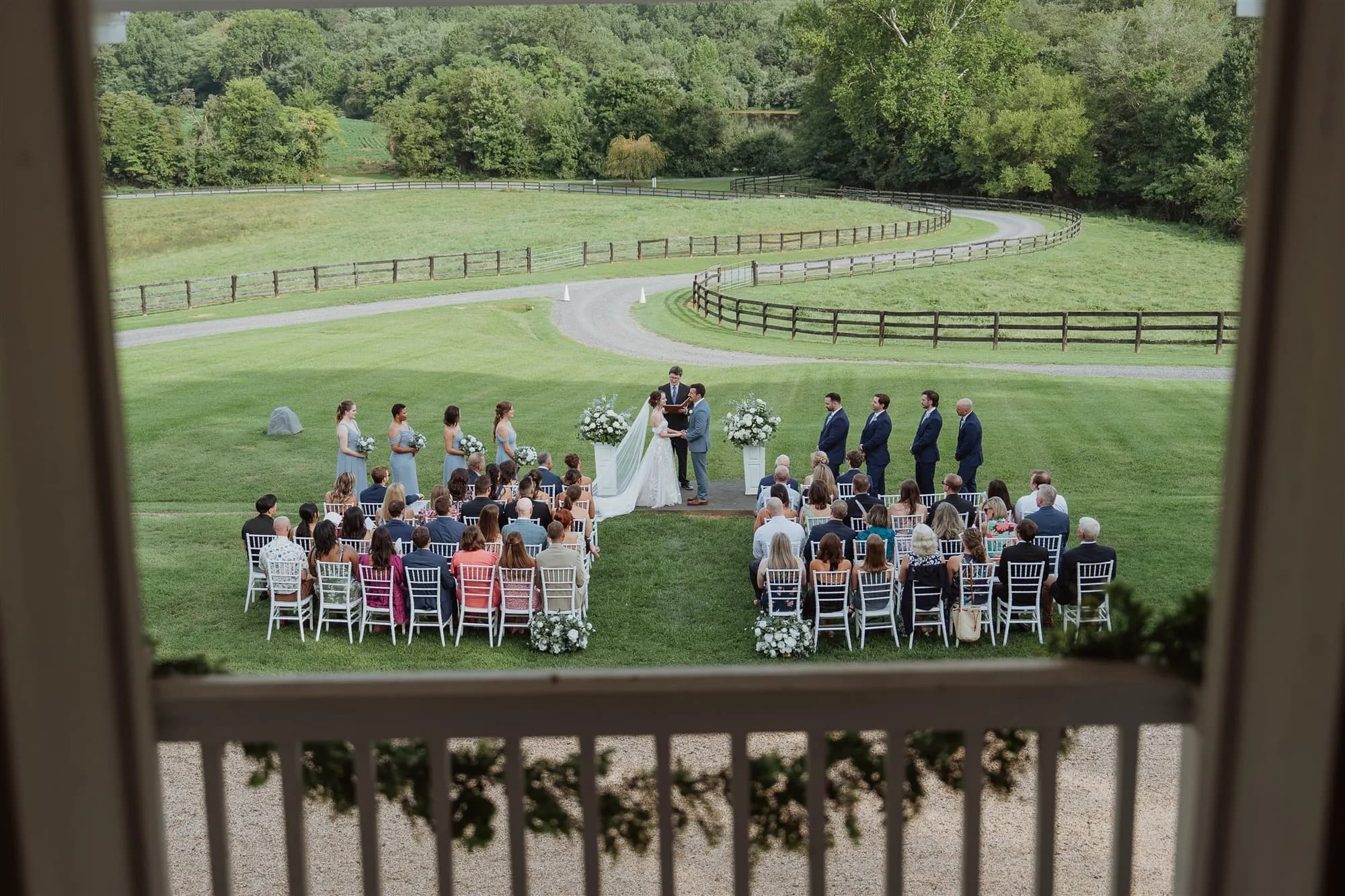 Wedding ceremony on manicured grounds with bride and groom exchanging vows, guests seated on either side.