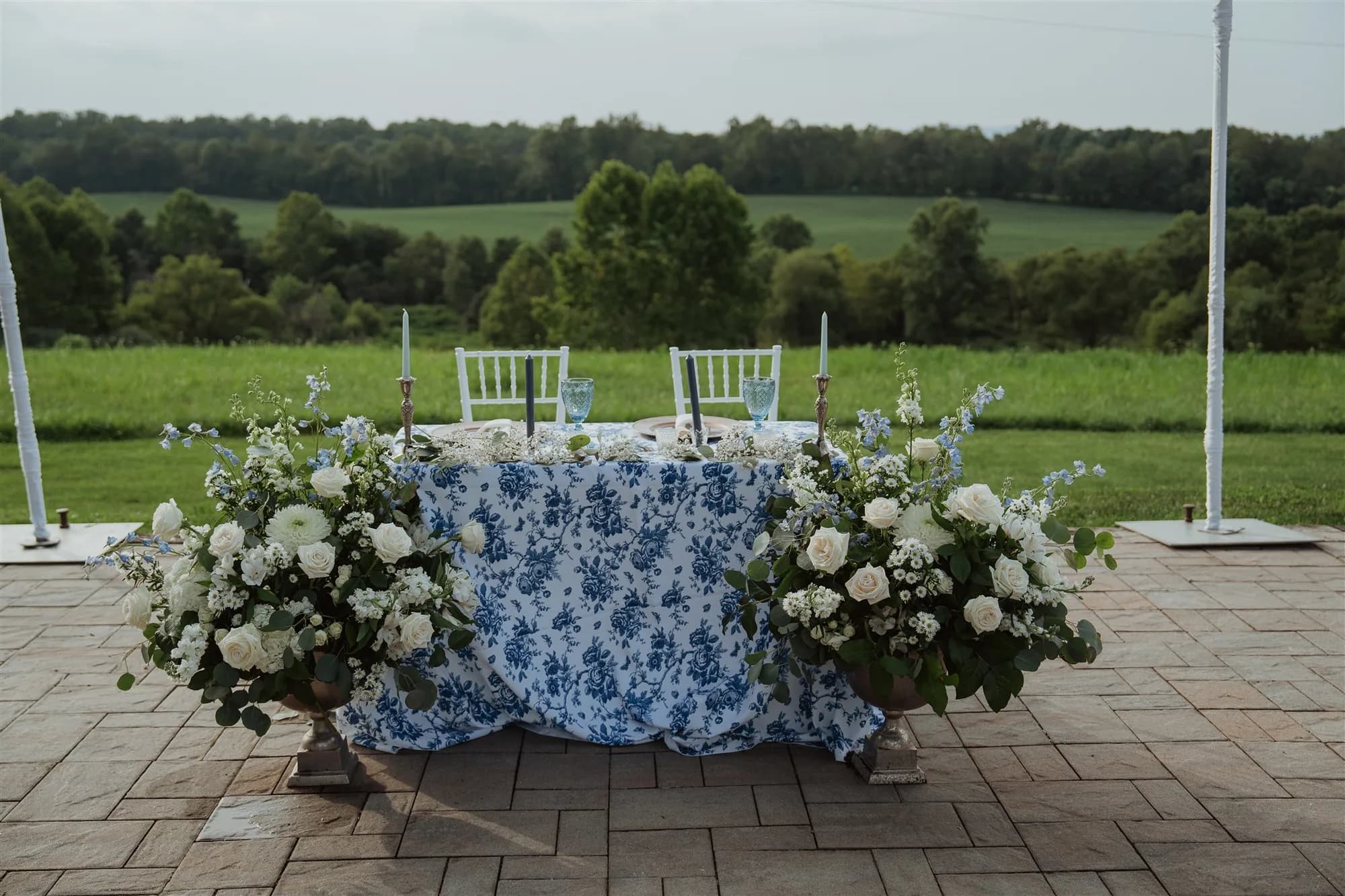 Sweetheart table with blue floral linens and white roses on Rixey Manor's stone terrace overlooking rolling Virginia fields