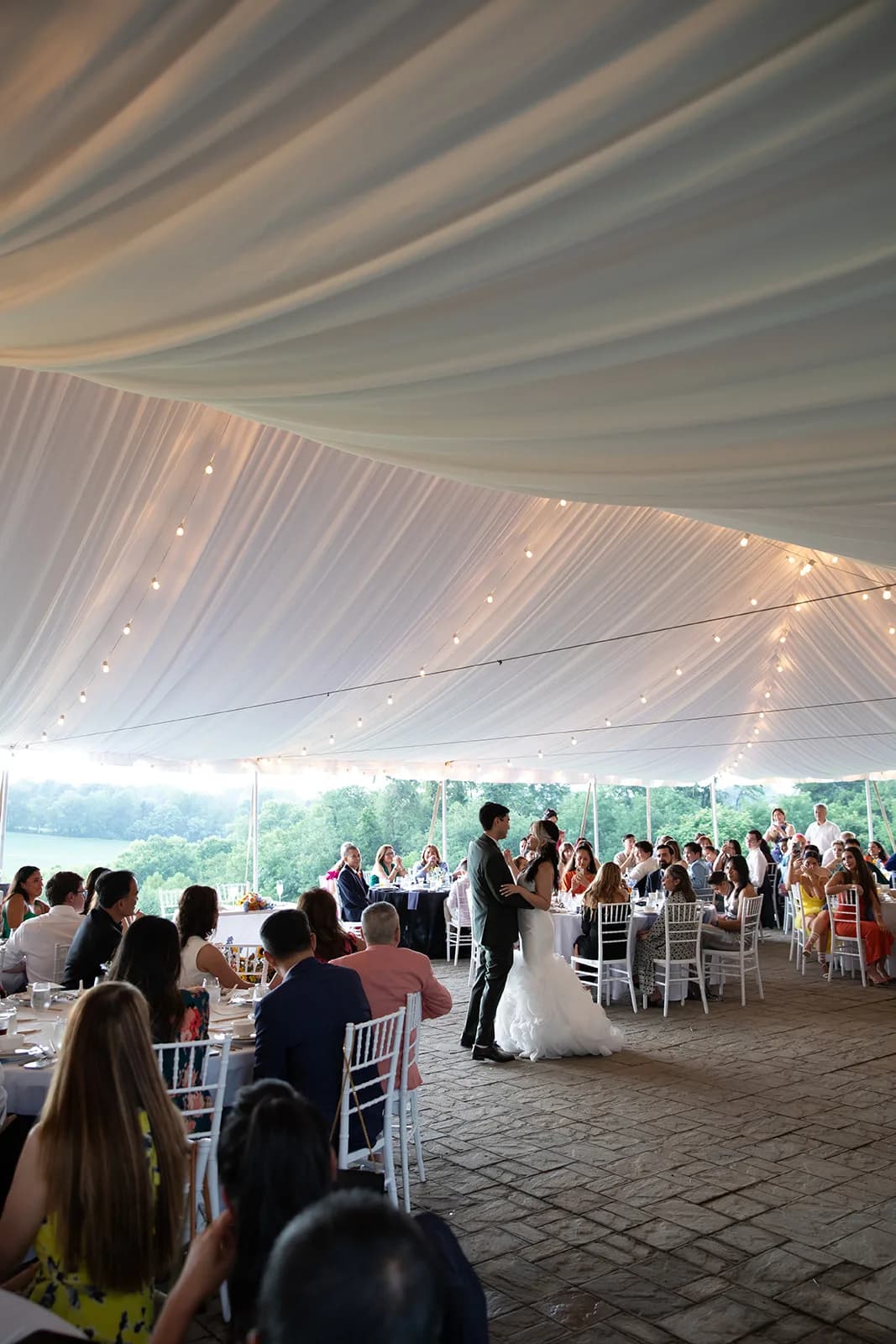 Bride and groom share first dance under draped tent with string lights and lush Virginia countryside at Rixey Manor reception