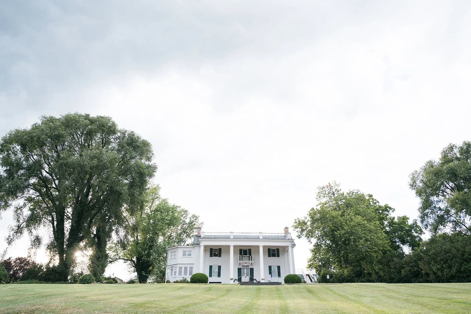 Wide view of Rixey Manor's white colonial estate facade surrounded by lush green trees and manicured lawn