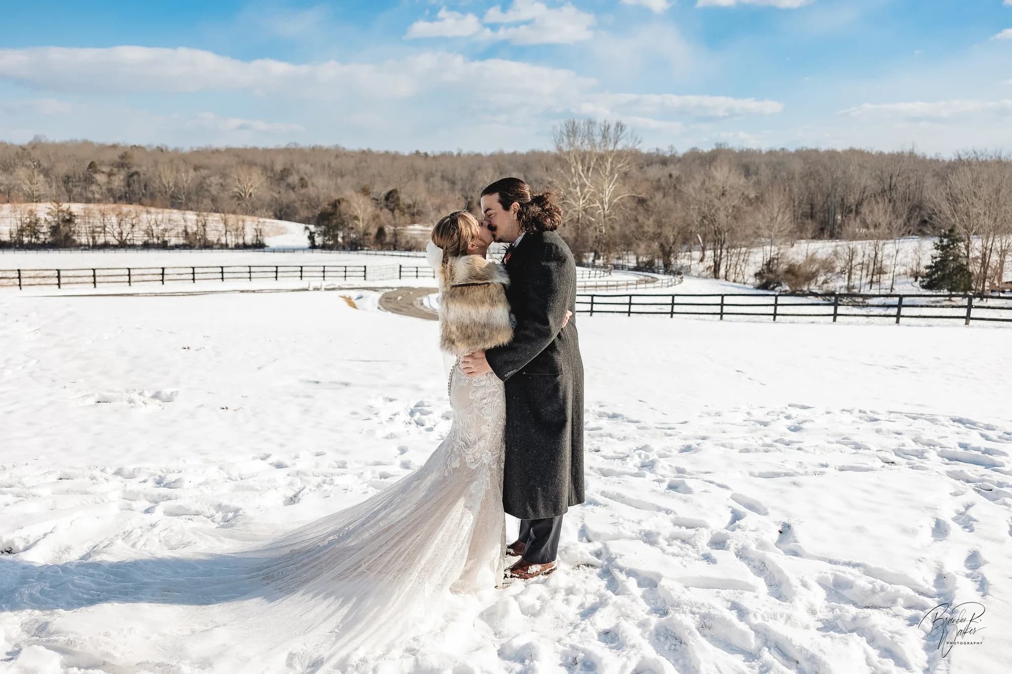 Bride and groom share a kiss in snow-covered Rixey Manor grounds, bride's lace train spreading across the field