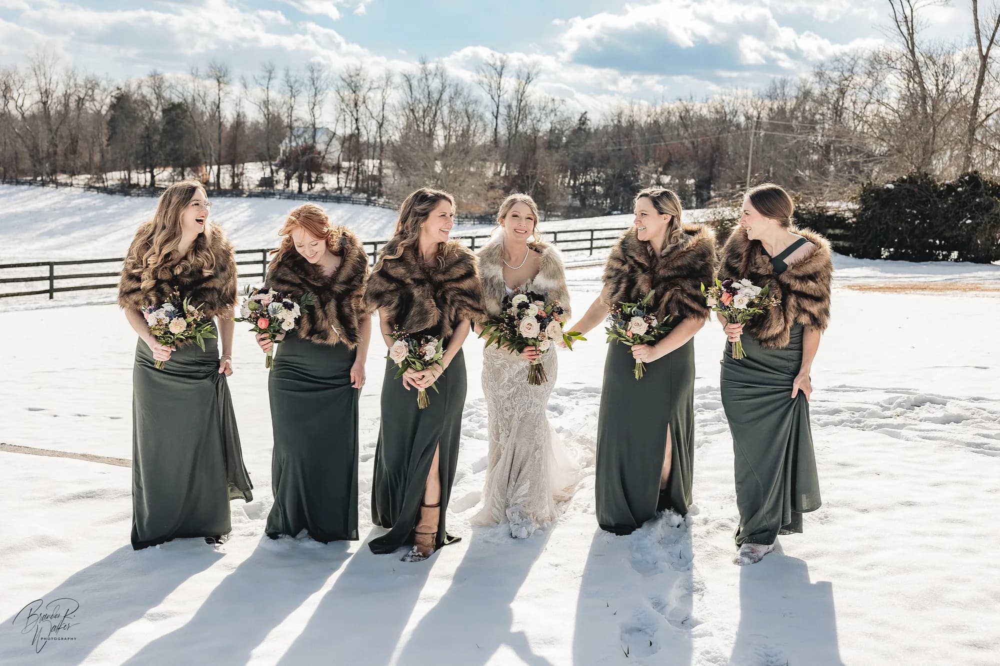 Bride and bridesmaids in fur wraps laugh together on snowy Rixey Manor grounds in winter