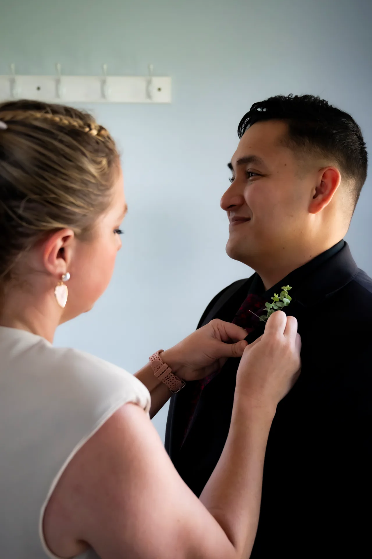 Bride pins boutonniere on smiling groom before wedding ceremony