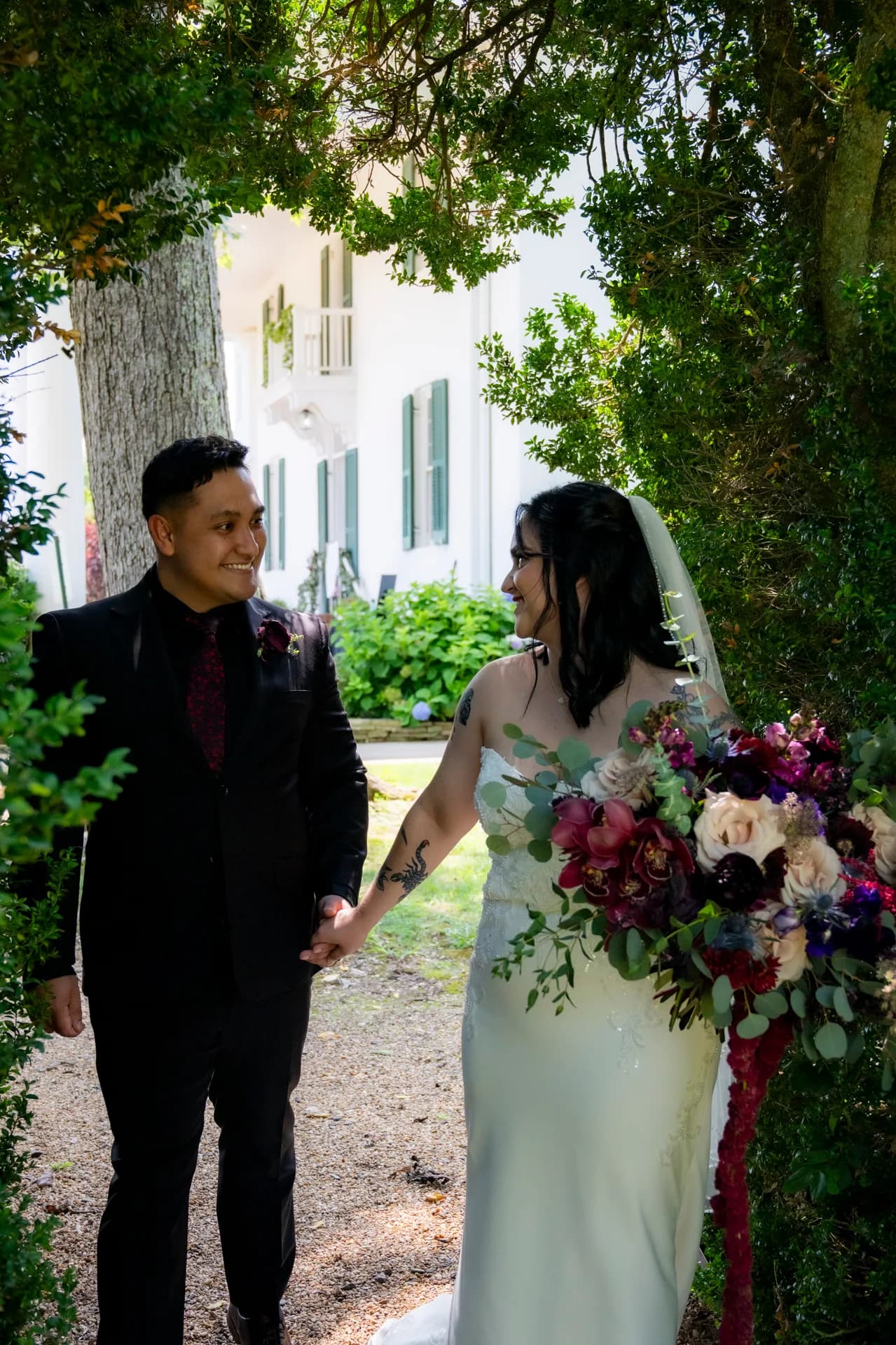 Bride and groom hold hands and smile at each other beneath lush trees at Rixey Manor estate
