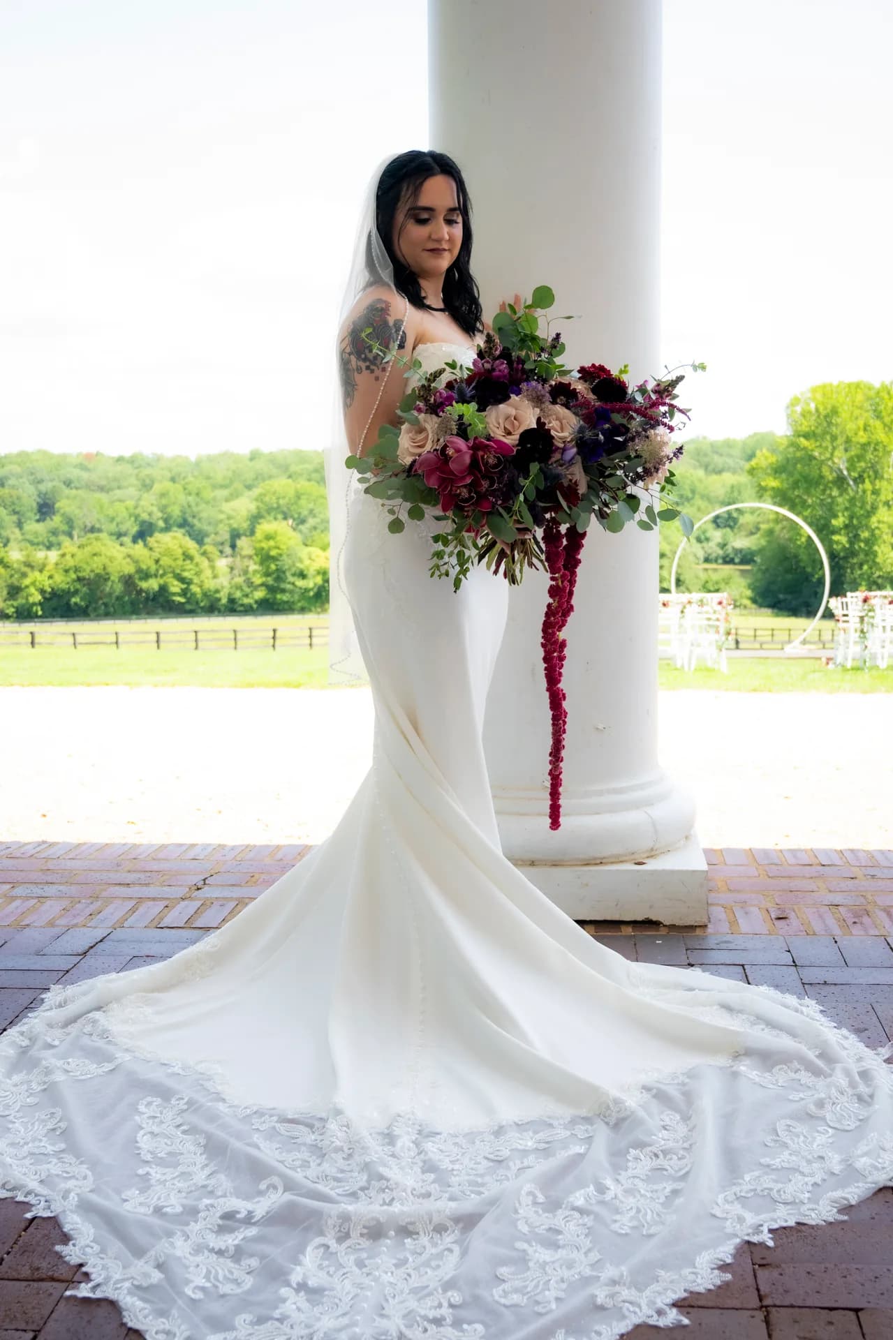 Bride in mermaid gown holding lush burgundy bouquet beside white column at Rixey Manor portico