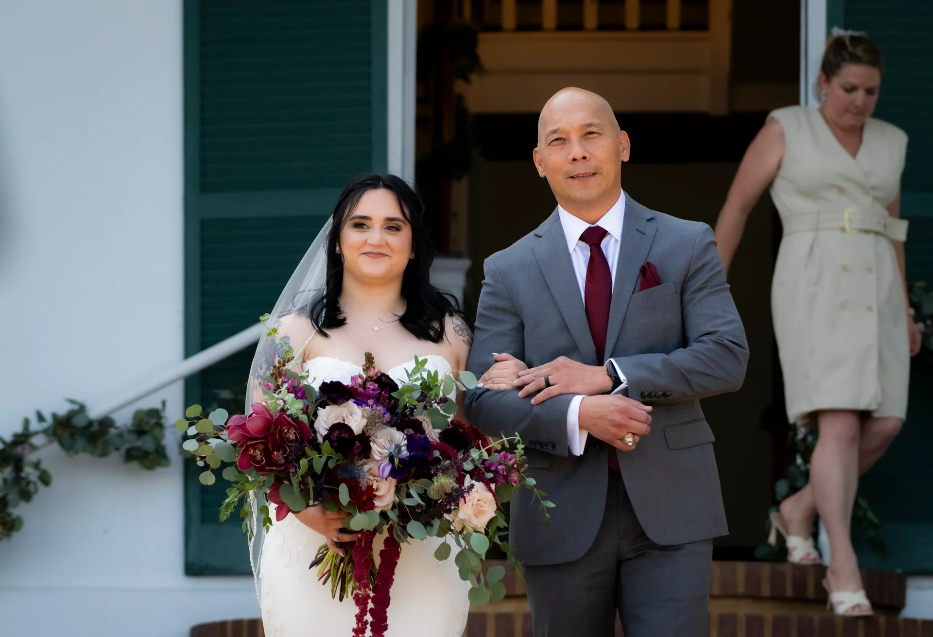 Bride and escort walk arm-in-arm before Rixey Manor's white colonial facade with green shutters