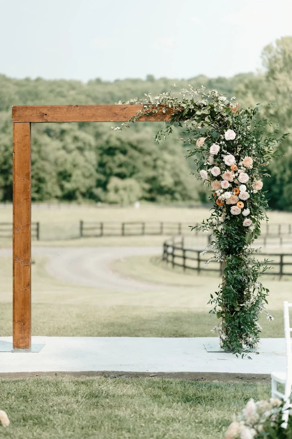 Rustic wooden ceremony arch adorned with lush greenery and blush florals on the open lawn at Rixey Manor