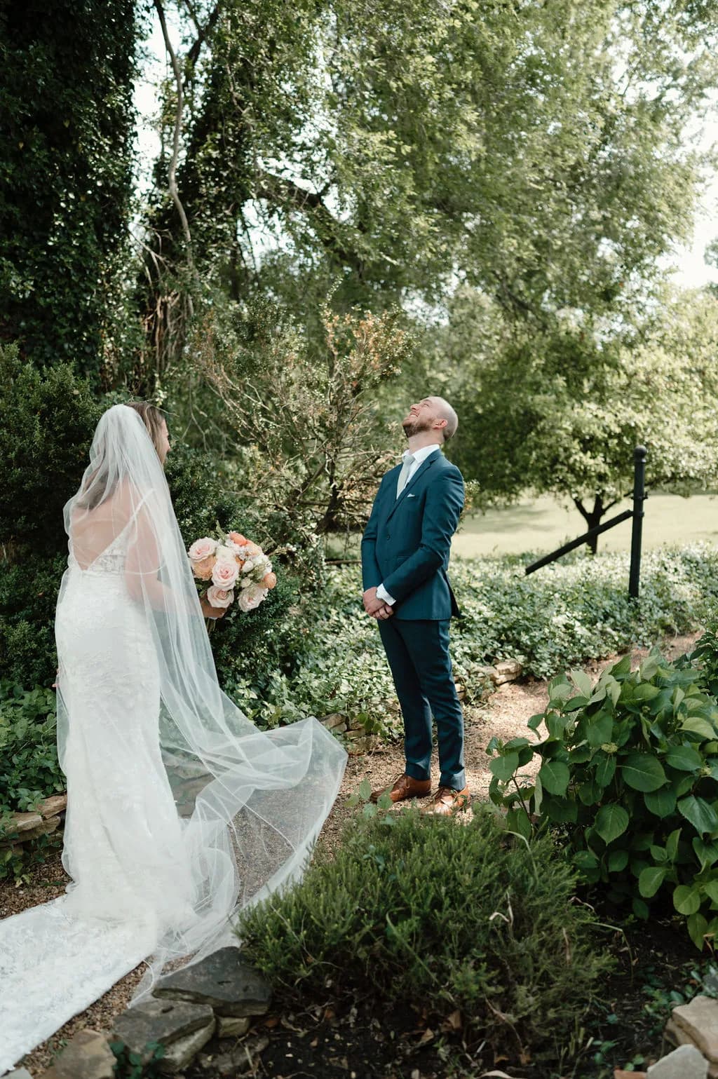 Groom looks skyward during first look with bride in lush garden grounds at Rixey Manor, Virginia