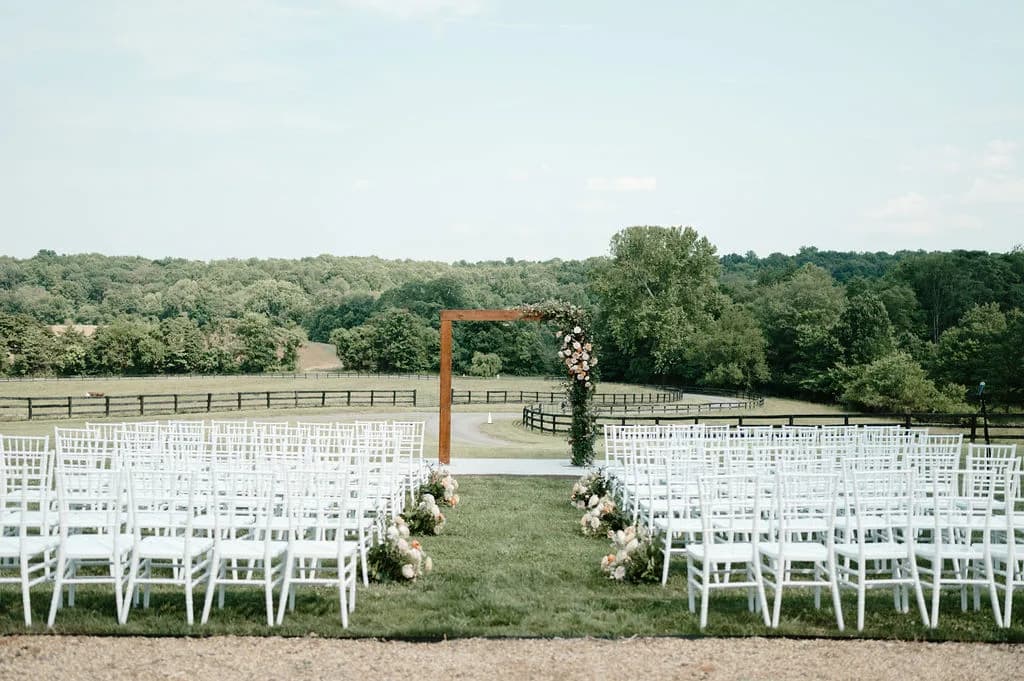 Outdoor ceremony setup with wooden arch, white chairs, and rolling Virginia countryside at Rixey Manor