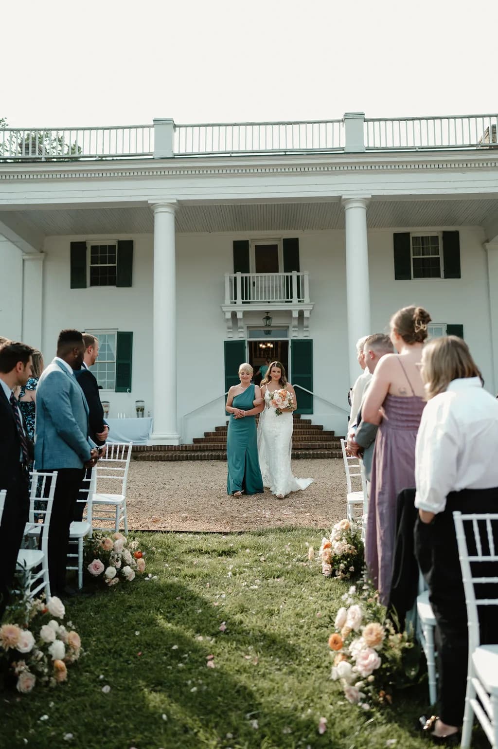 Bride walks down the aisle with escort before Rixey Manor's white columned facade during outdoor ceremony