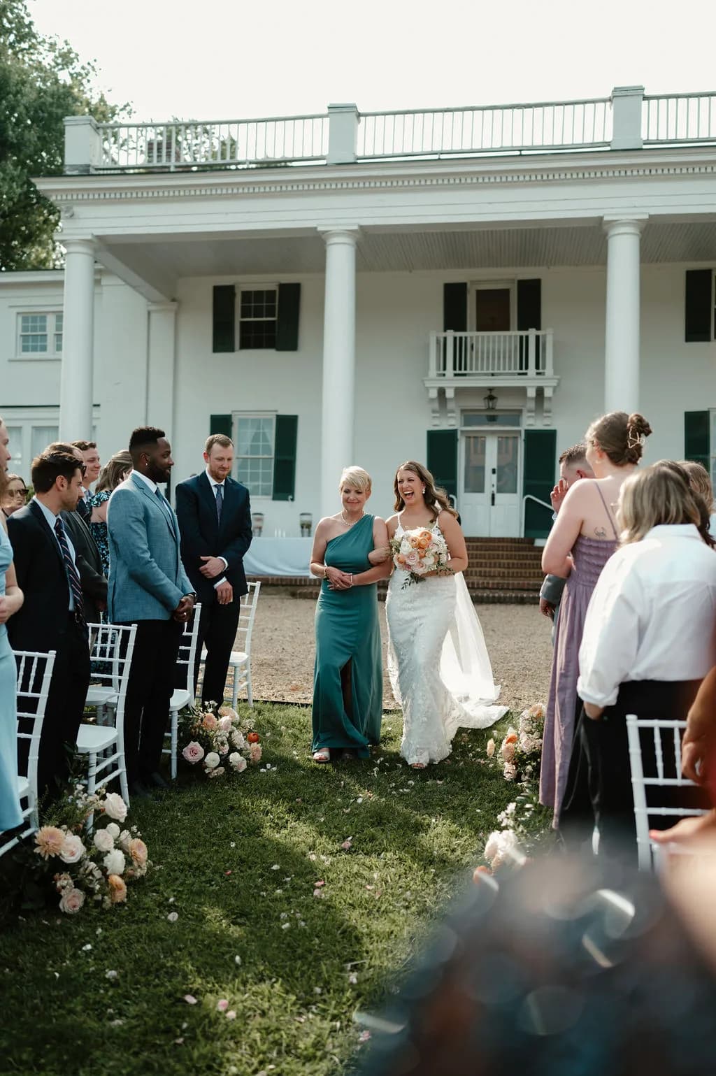 Outdoor wedding ceremony at white manor with bride, groom, and guests on manicured lawn