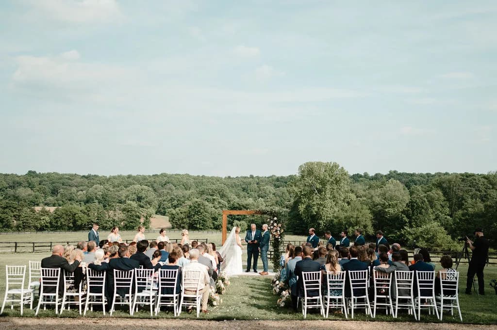 Wide aerial view of outdoor wedding ceremony on Rixey Manor grounds with wooded Virginia countryside backdrop
