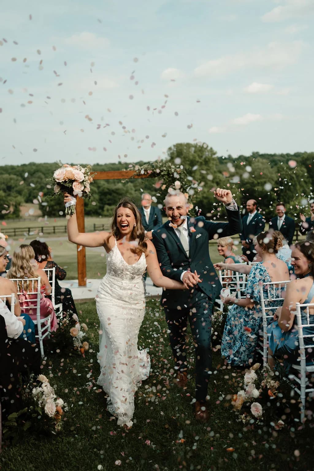 Bride and groom walk back down the aisle at Rixey Manor as guests toss confetti at outdoor ceremony