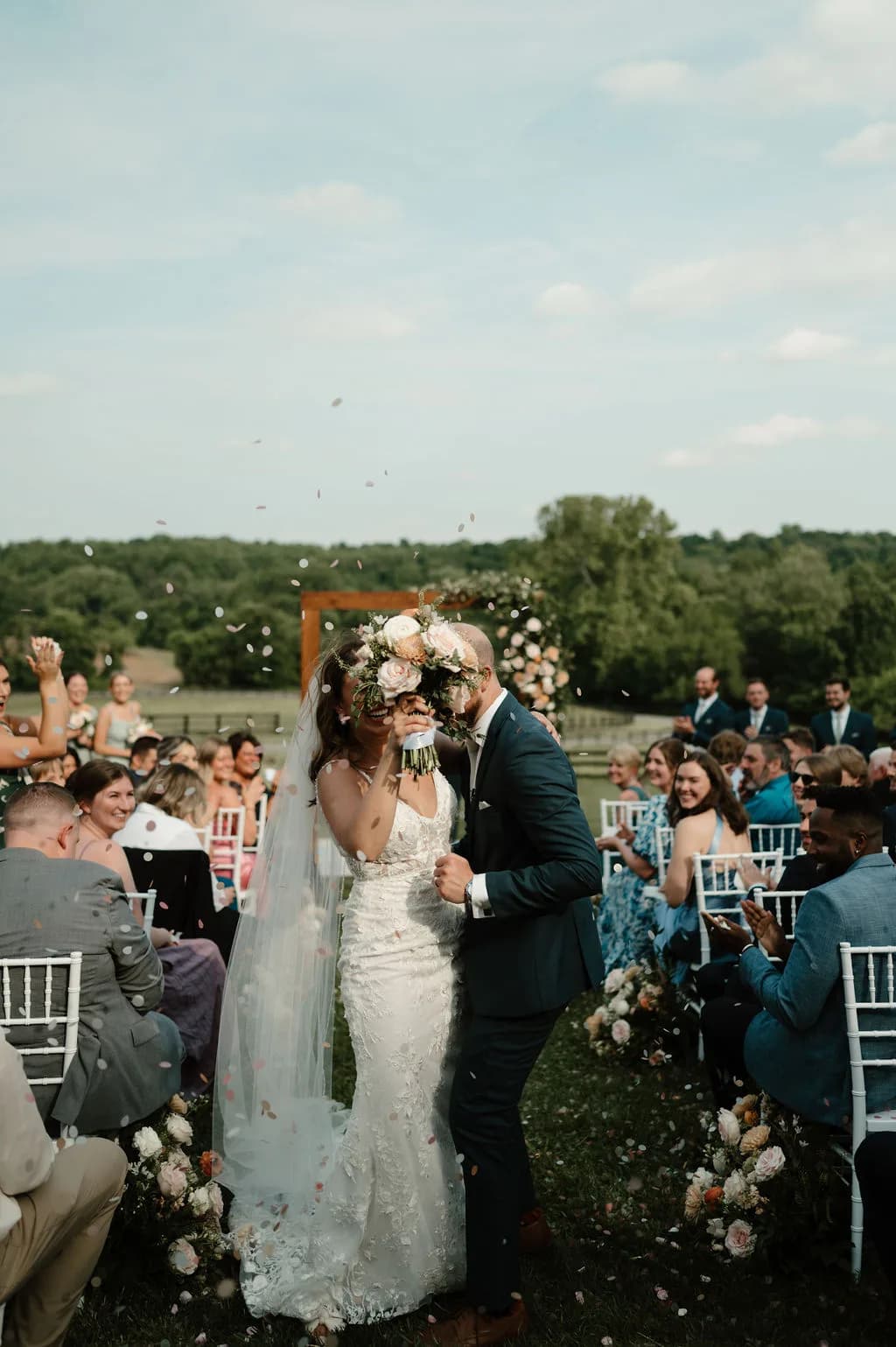 Newlyweds share first kiss at outdoor ceremony aisle as guests toss confetti at Rixey Manor