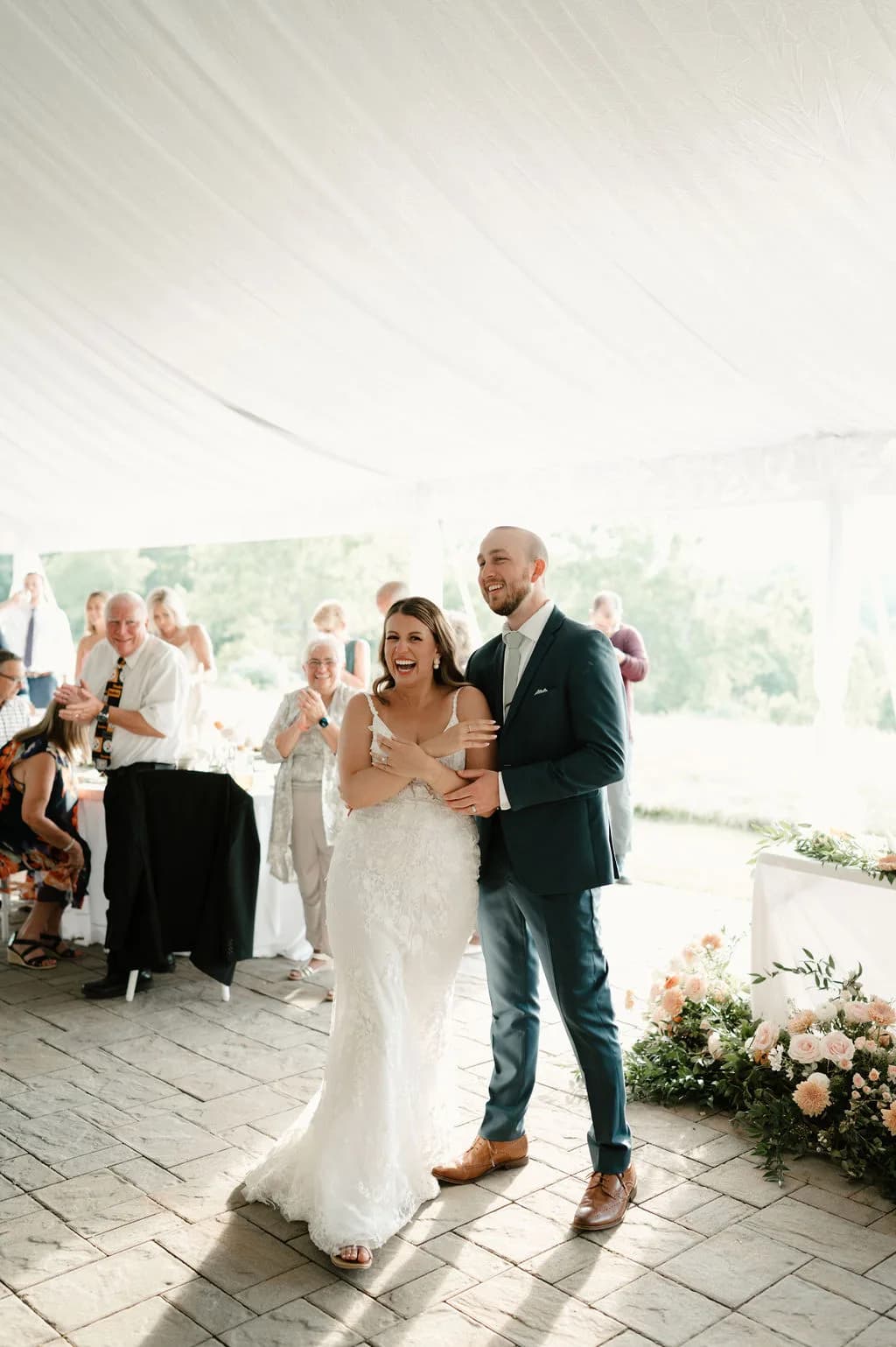 Laughing bride and groom share first dance under white tent at Rixey Manor with guests celebrating behind them