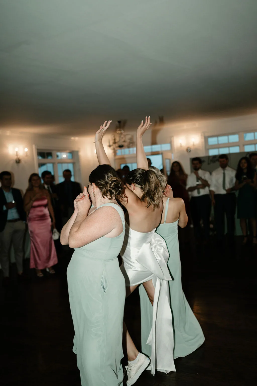 Two brides dancing together at their wedding reception with guests watching in the background.