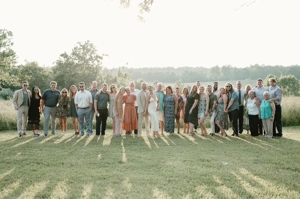 Large wedding party group photo on a grass field with trees in soft afternoon light