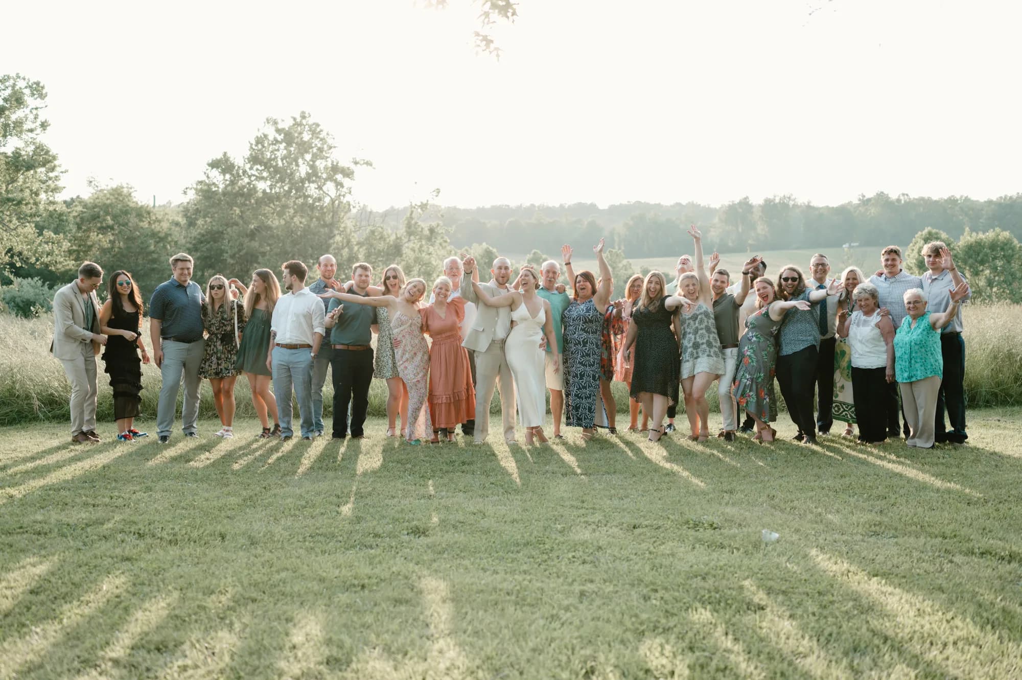 Large wedding party celebrates on Rixey Manor lawn at golden hour with rolling Virginia countryside behind them.