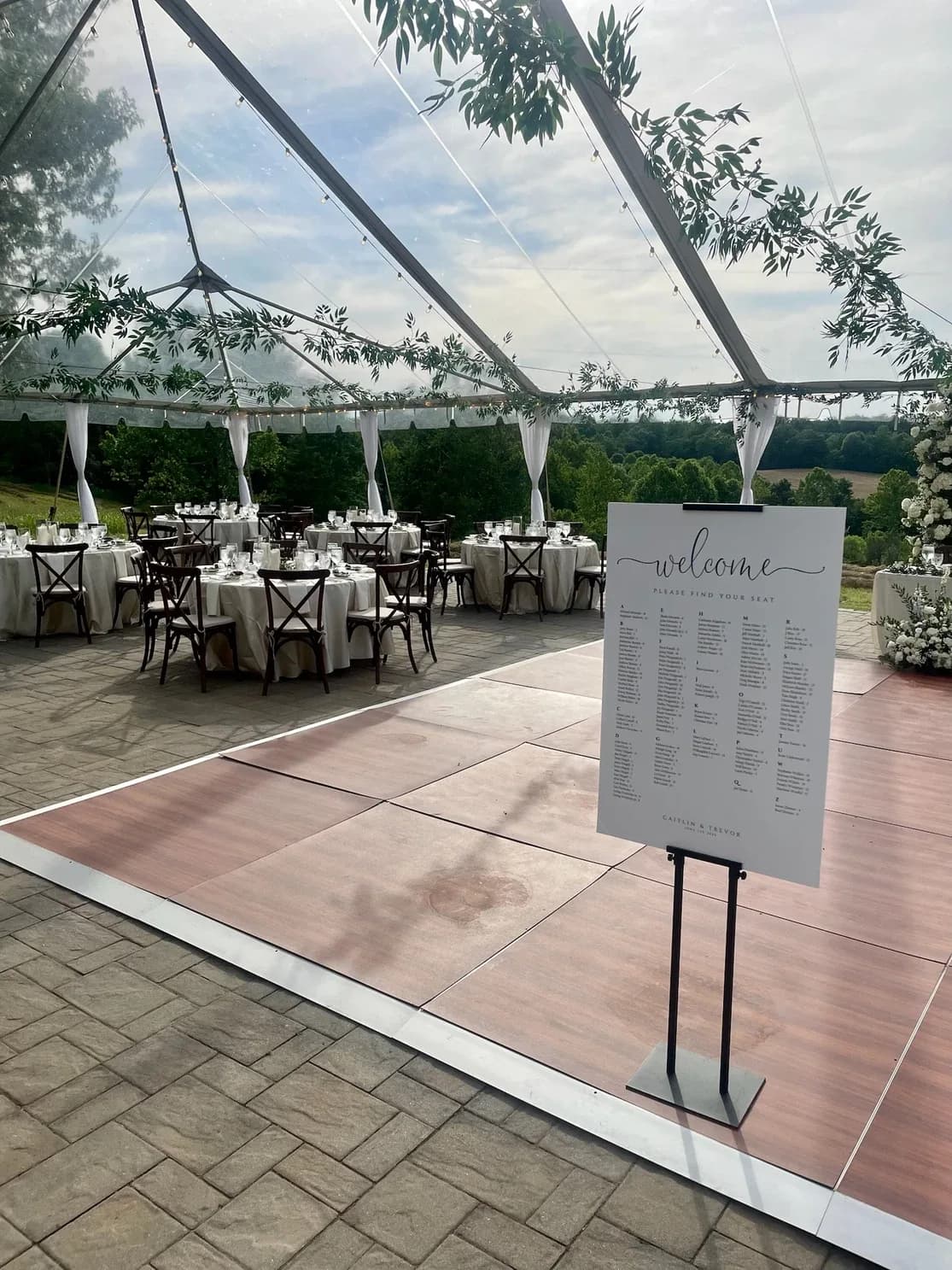 Welcome seating chart sign on dance floor inside Rixey Manor's clear-top tent with rural Virginia views