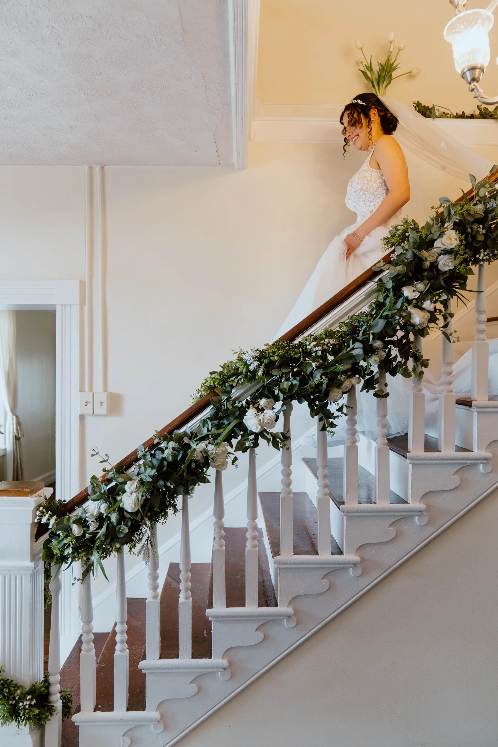 Bride smiling on garland-draped staircase inside Rixey Manor's grand historic foyer
