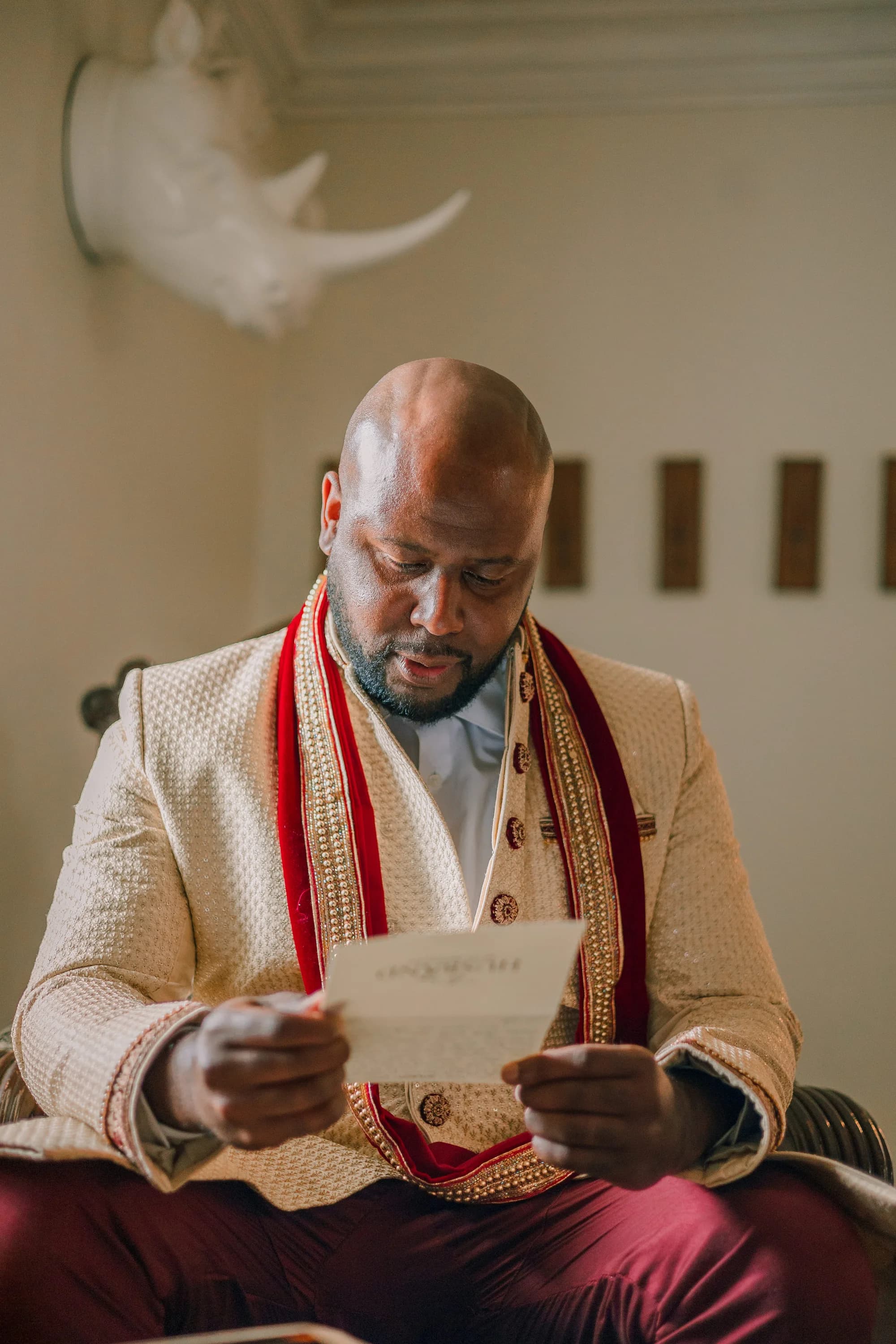 Groom in ornate cream and red sherwani reads a heartfelt letter before his wedding ceremony