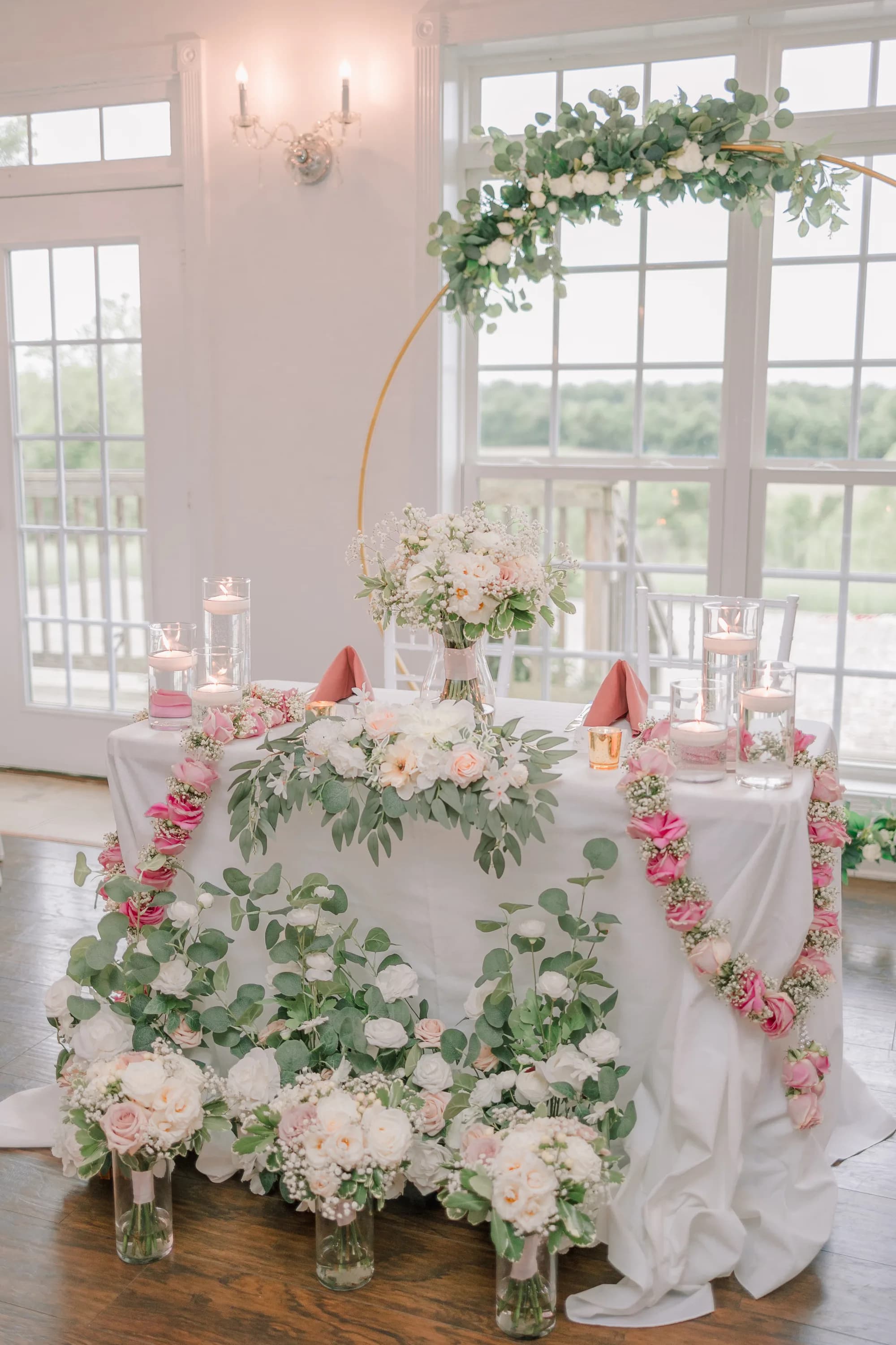 Sweetheart table with white linens, pink and white florals, and gold arch at Rixey Manor