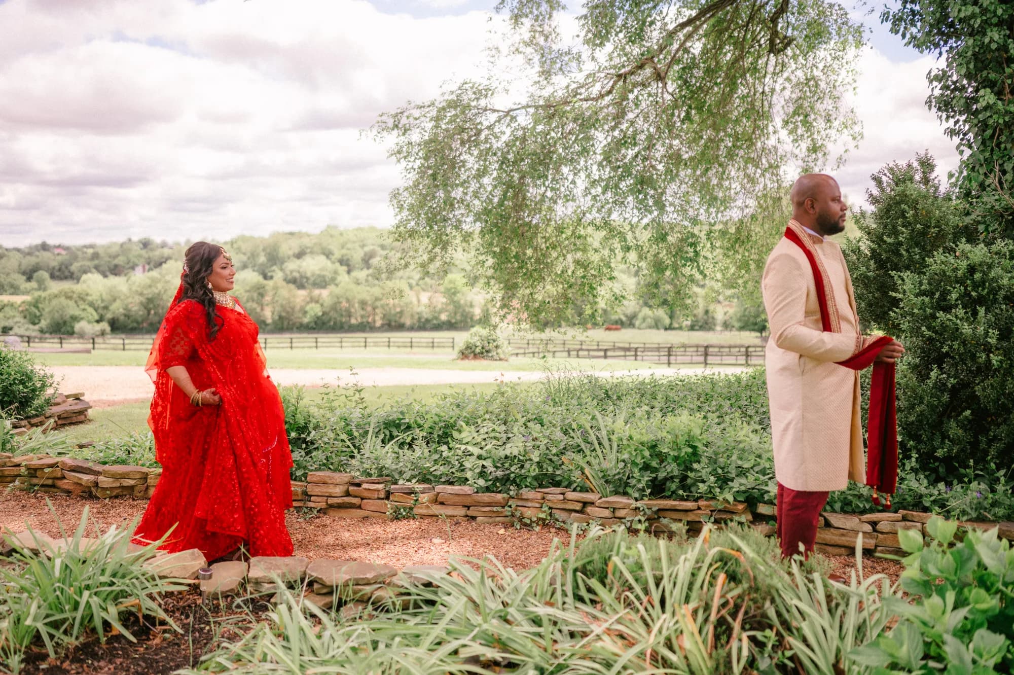Indian couple in traditional red and gold attire during first look moment in Rixey Manor garden grounds