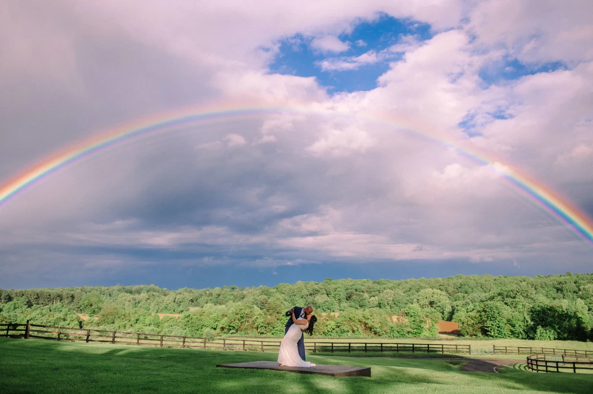 Couple sharing a romantic dip kiss beneath a stunning double rainbow over Rixey Manor's lush green grounds