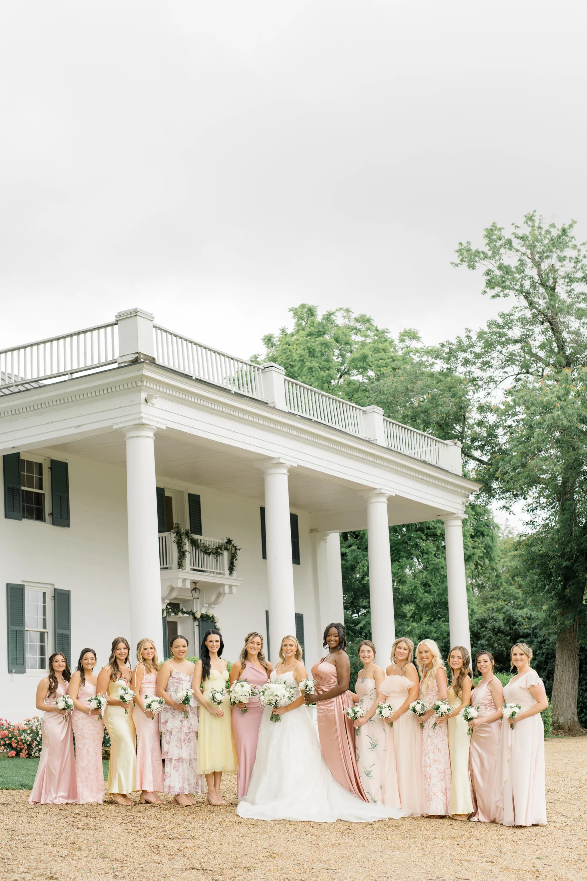 Bride and bridesmaids in pastel gowns pose before Rixey Manor's white columned facade