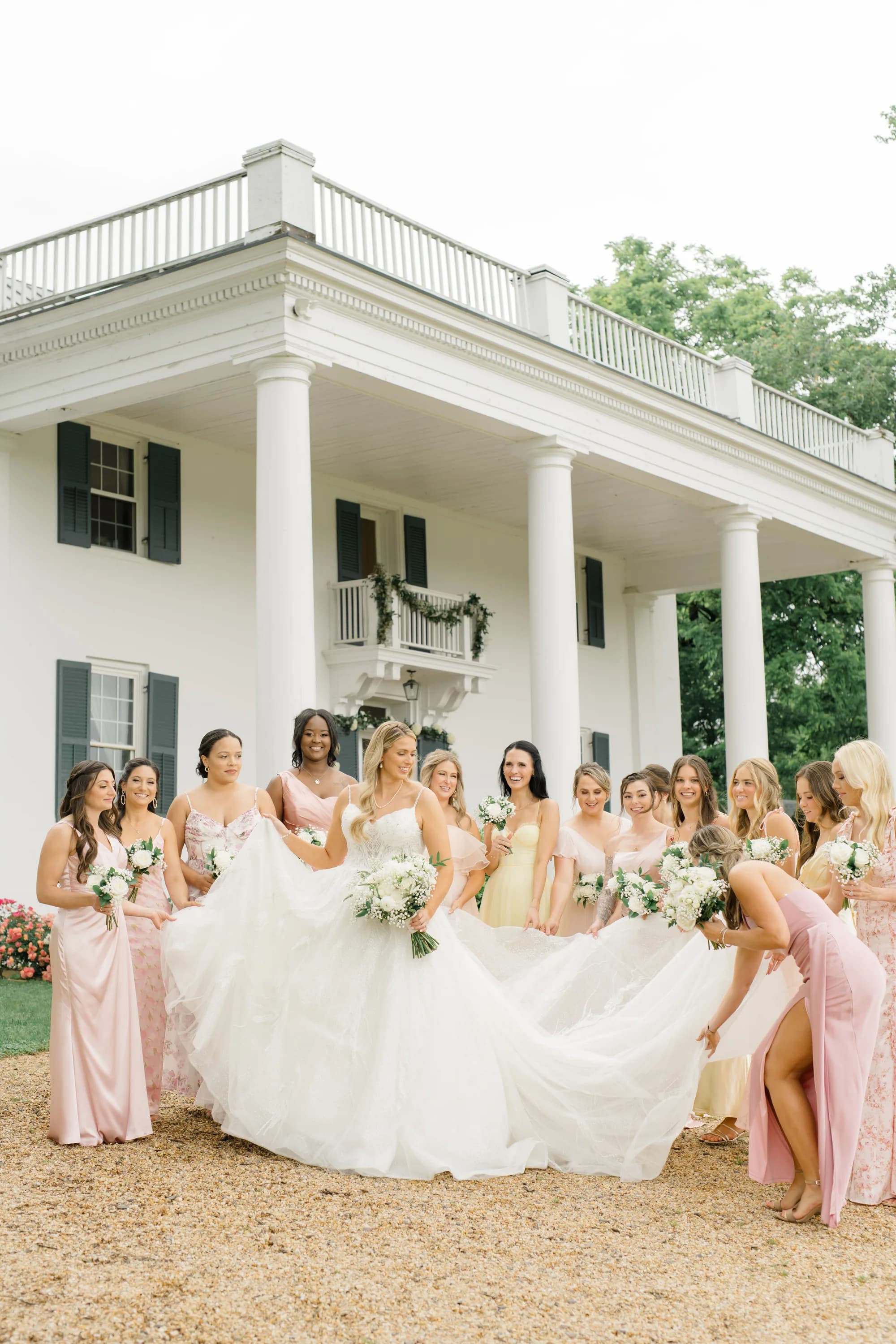 Bride and bridesmaids in pink dresses laugh outside Rixey Manor's white columned facade