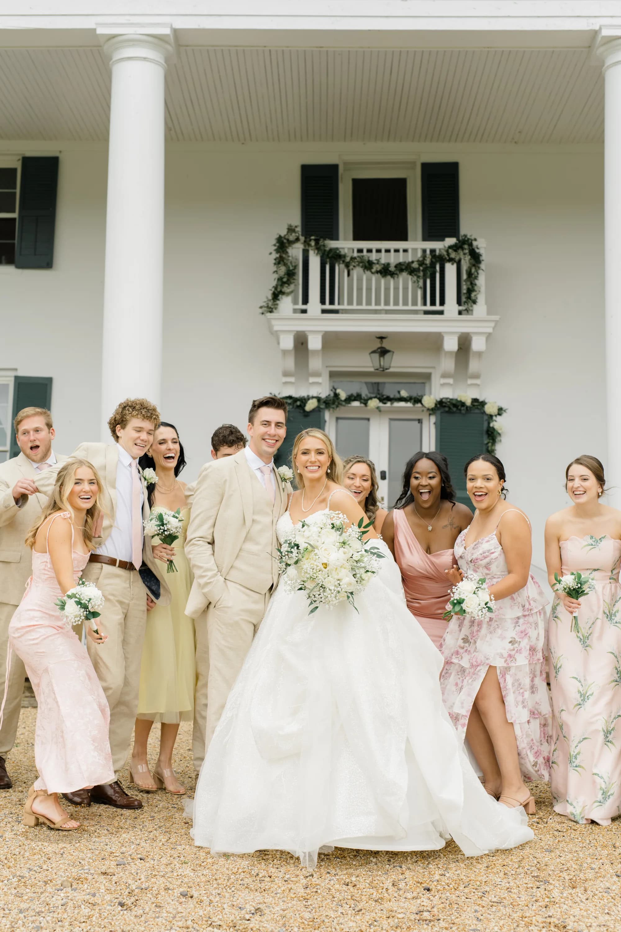 Bride and groom laugh with wedding party outside Rixey Manor's white columned facade