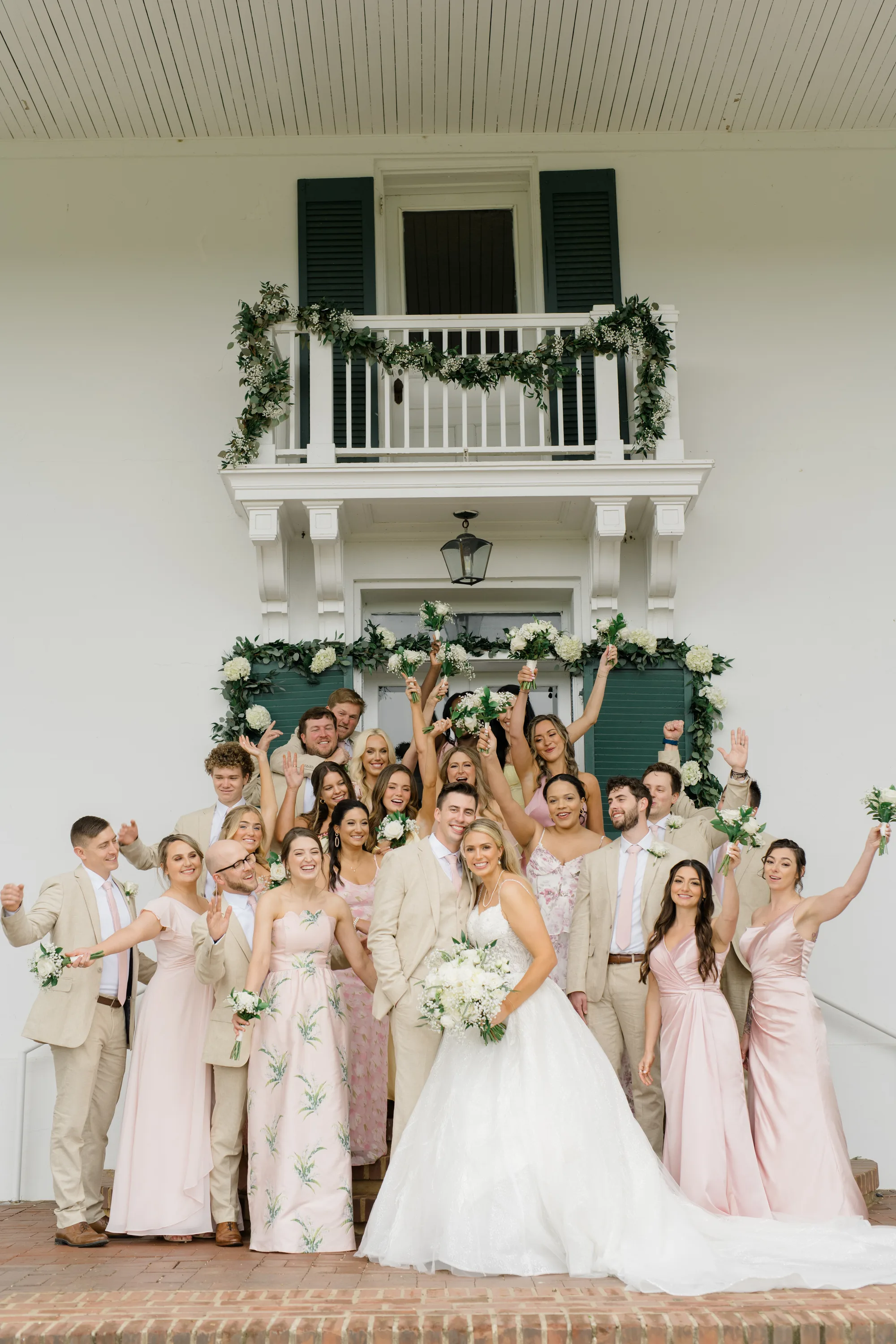 Joyful wedding party celebrating on steps of Rixey Manor's white columned entrance with greenery garland