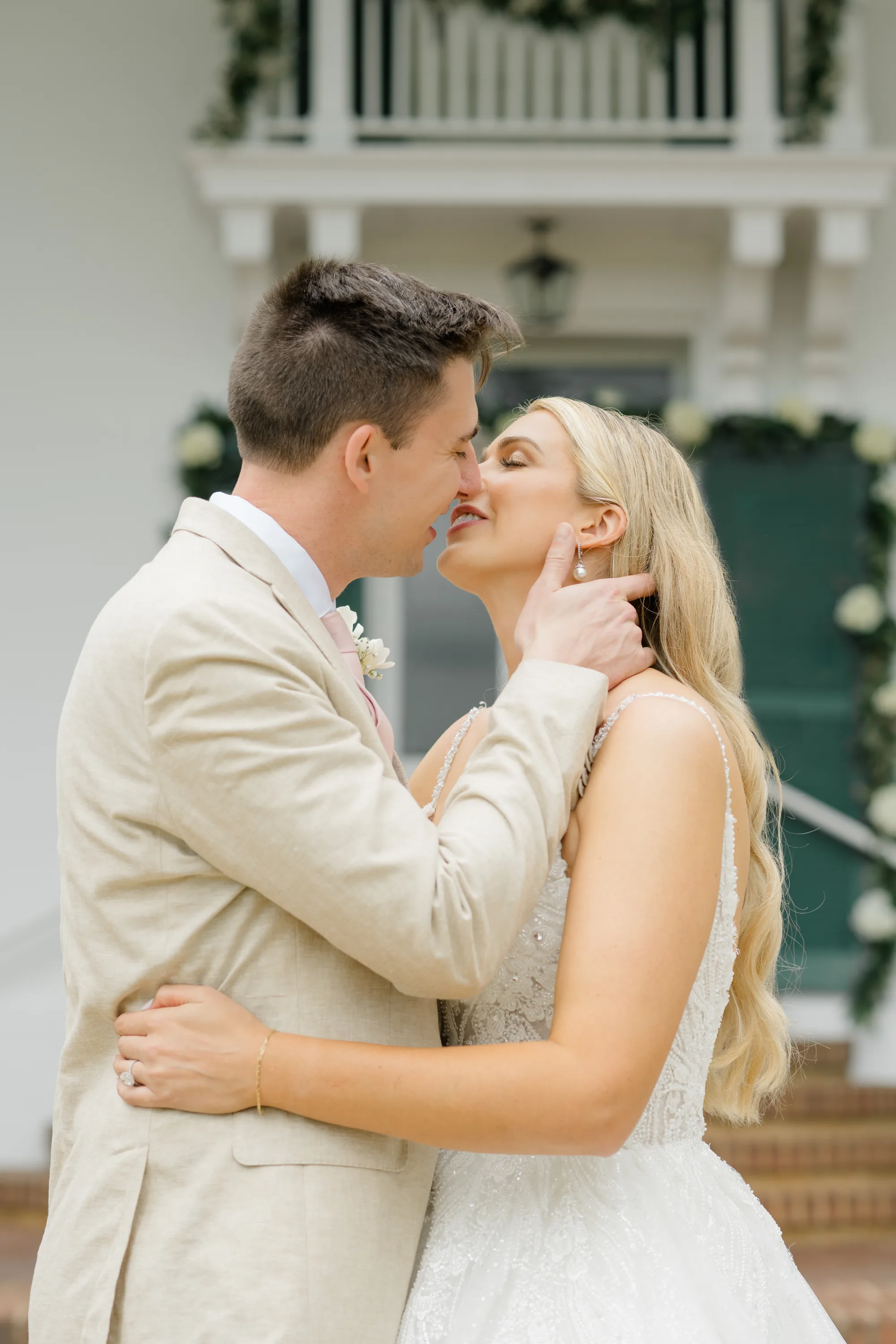 Bride and groom share a tender kiss in front of Rixey Manor's white columned facade with green floral accents