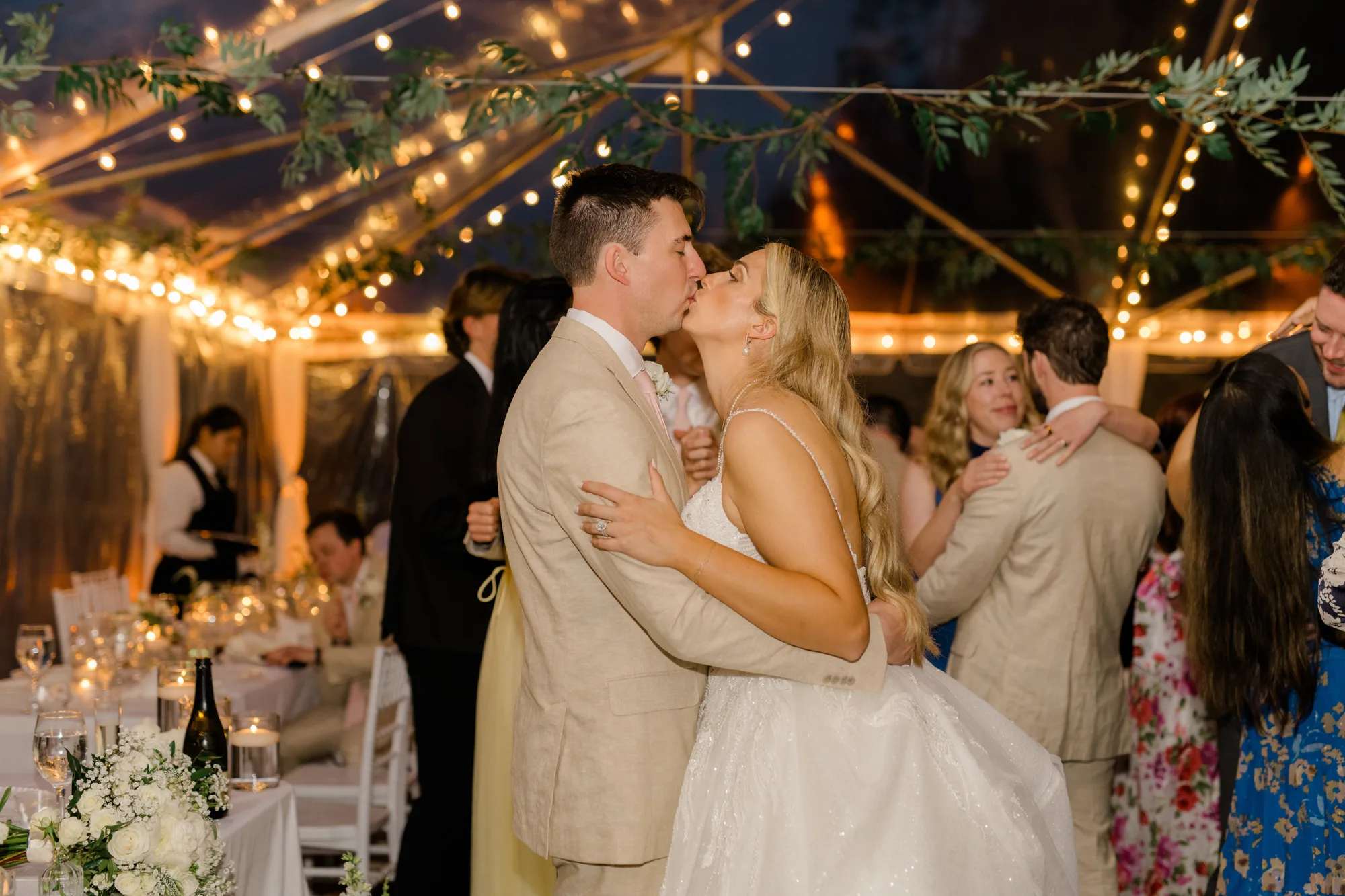 Bride and groom share a kiss on the dance floor under string lights in Rixey Manor's clear-top reception tent
